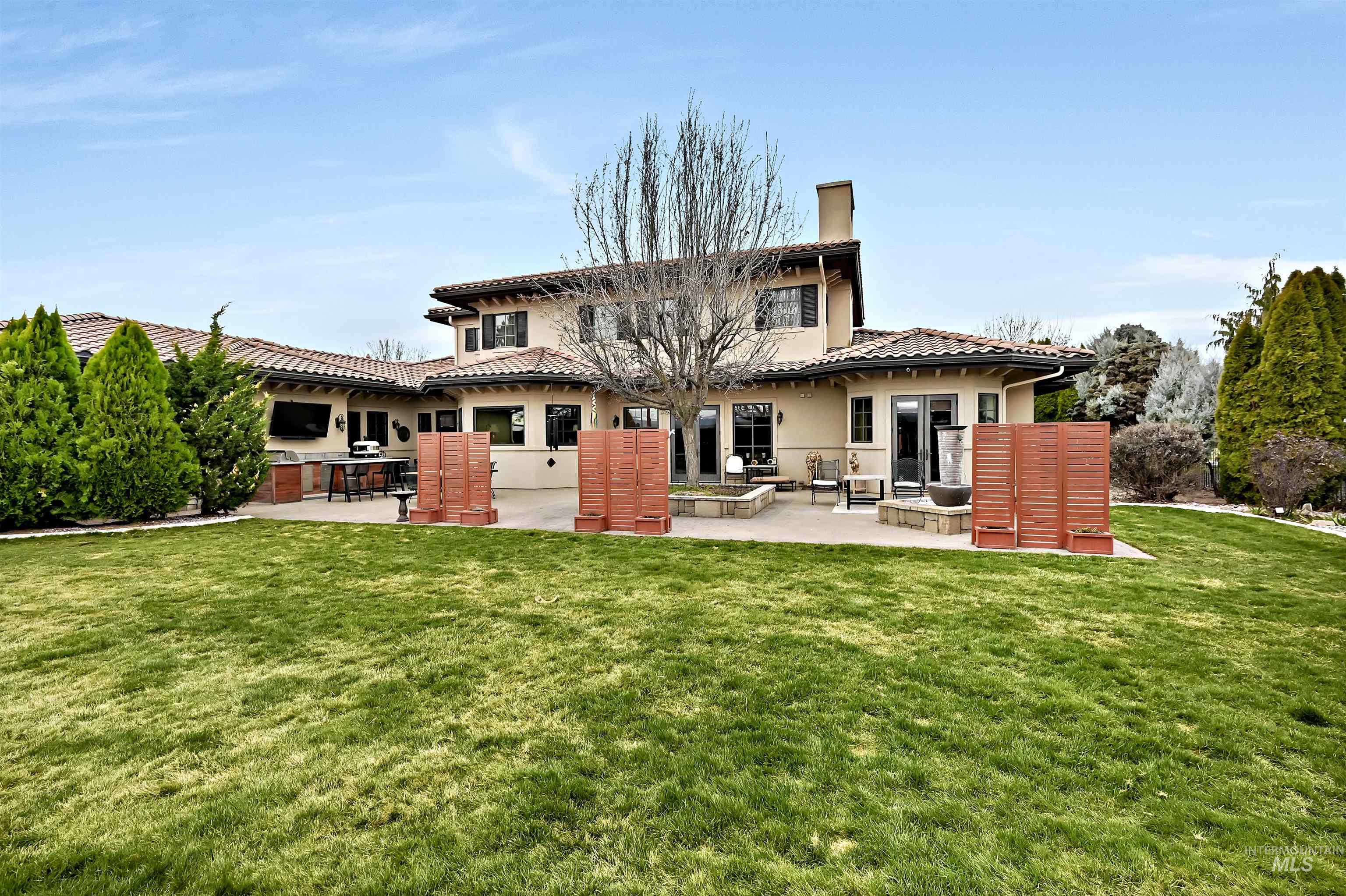 Back of house featuring a patio area, a lawn, a chimney, a tile roof, and stucco siding