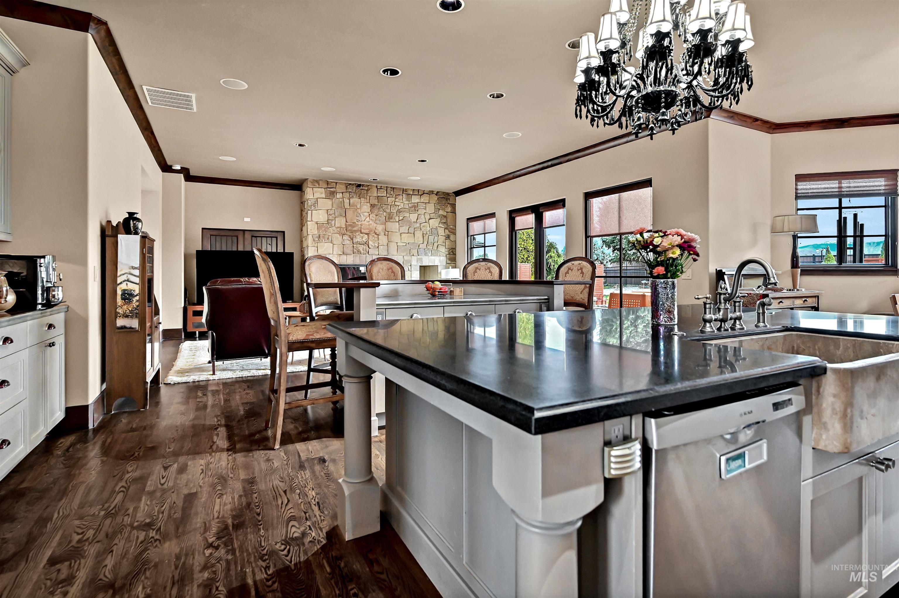 Kitchen with dishwasher, a center island with sink, dark wood-style floors, crown molding, and decorative chandelier