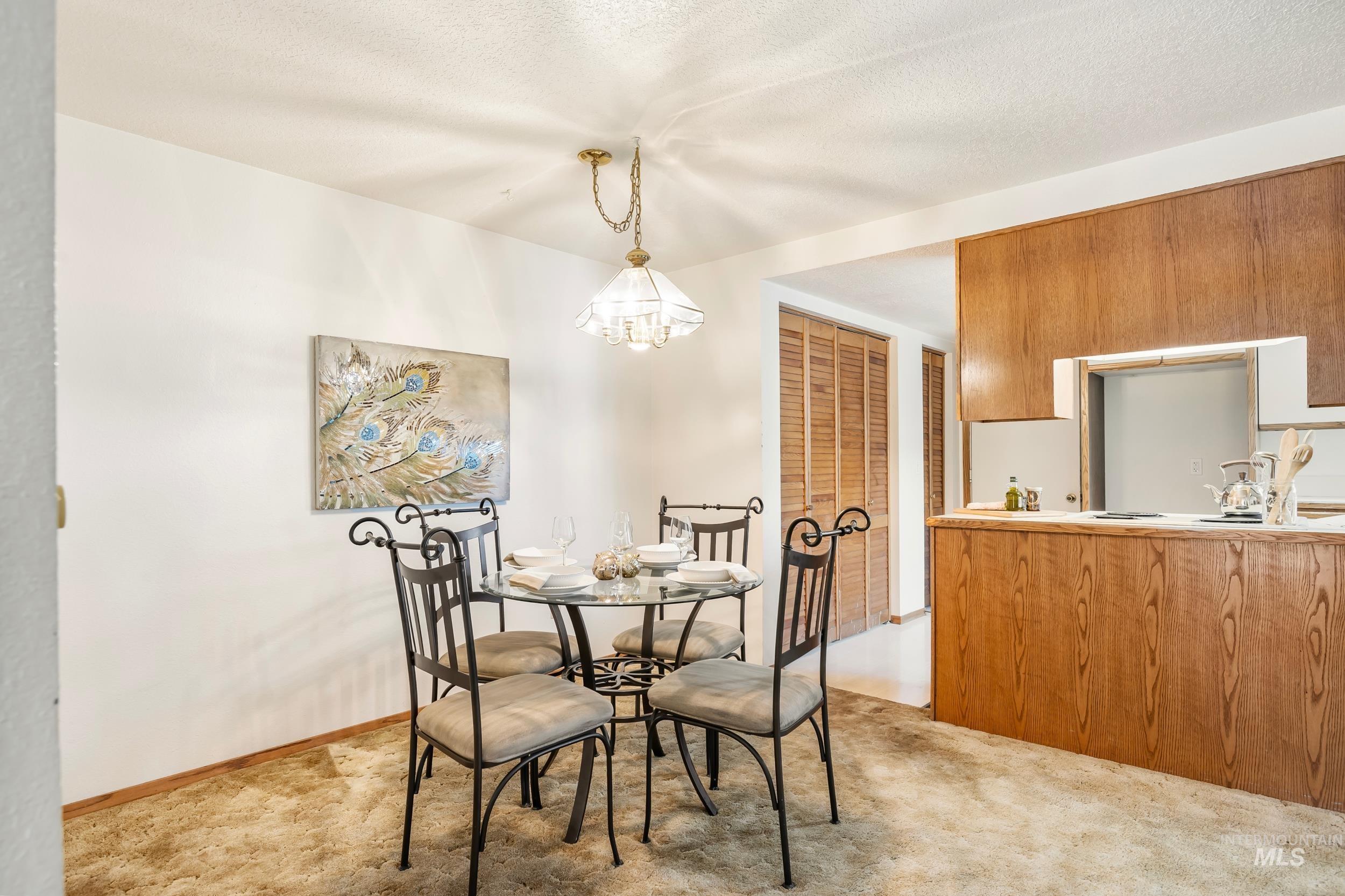 Dining space with light colored carpet, a chandelier, and a textured ceiling