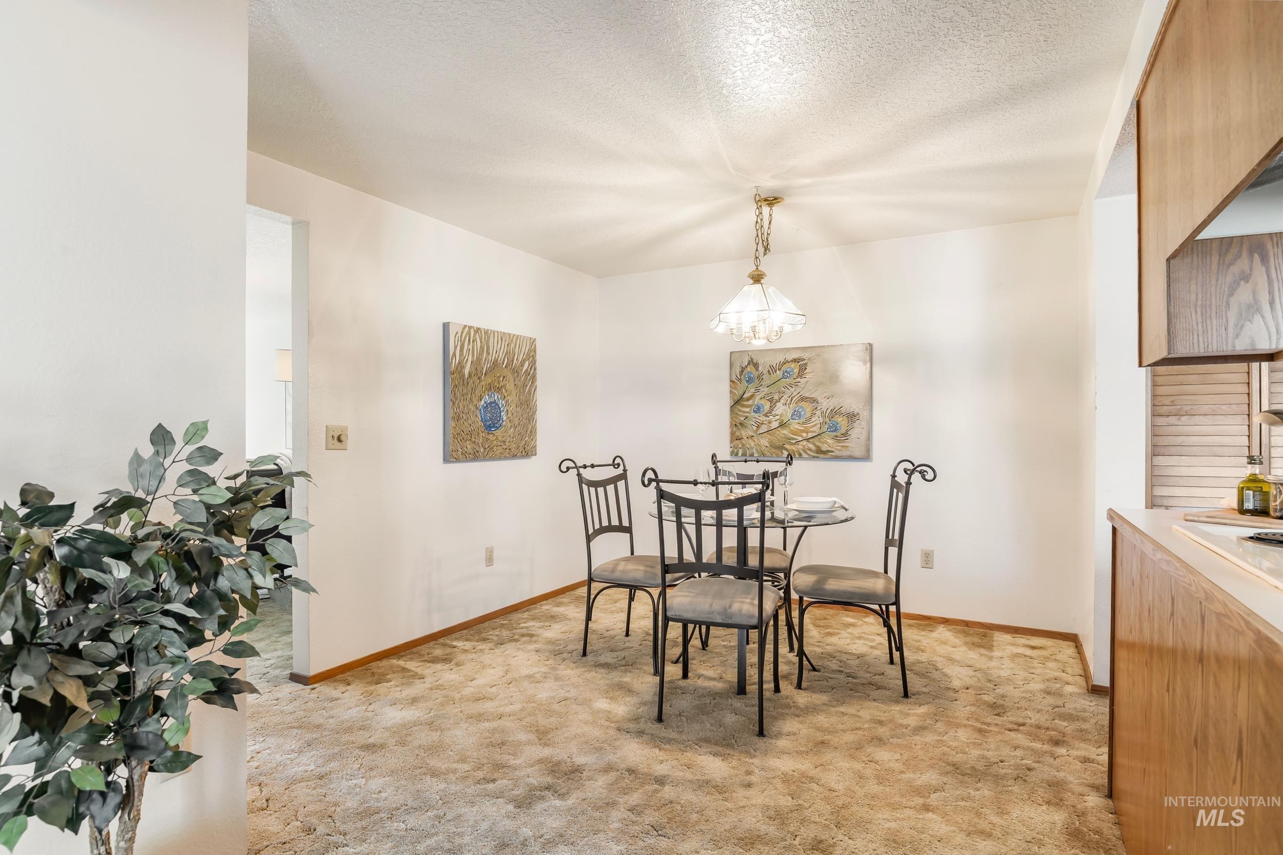 Dining space featuring light colored carpet, a chandelier, and a textured ceiling