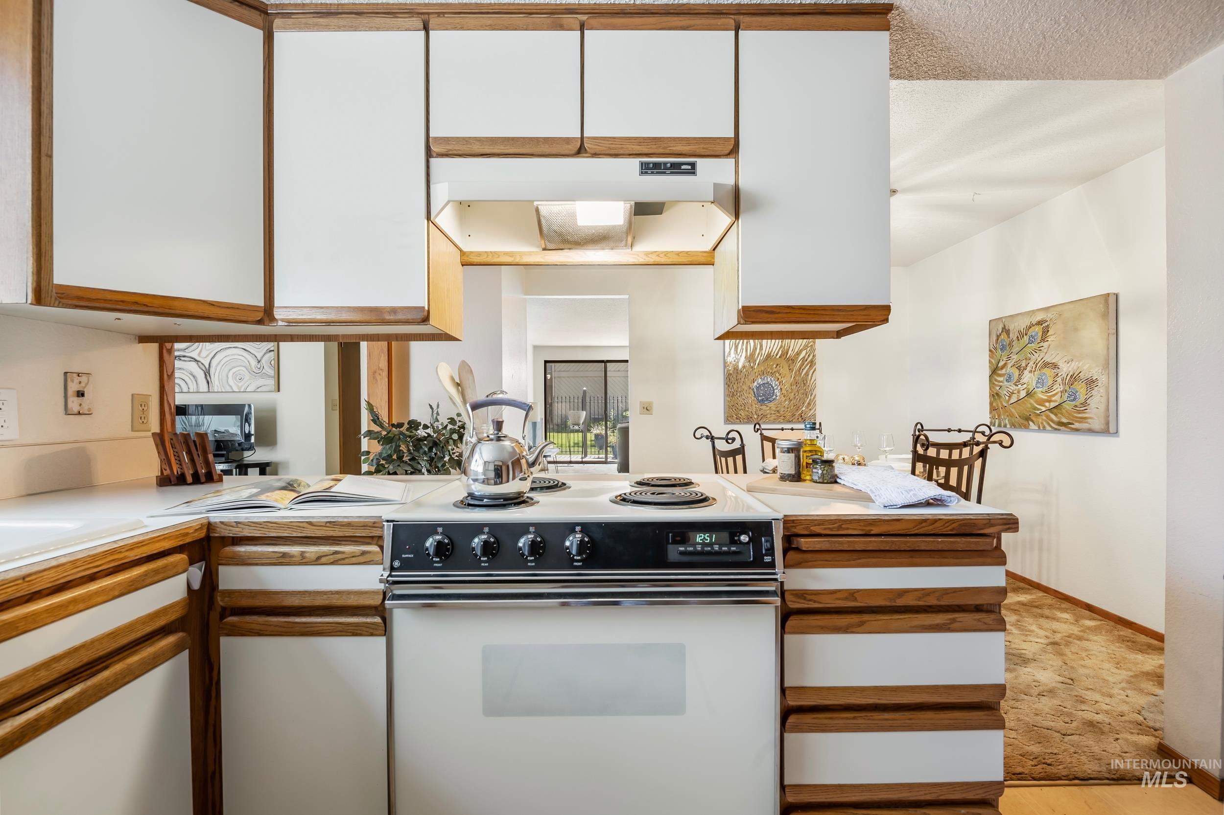 Kitchen with electric range, white cabinetry, light countertops, under cabinet range hood, and light wood-style floors