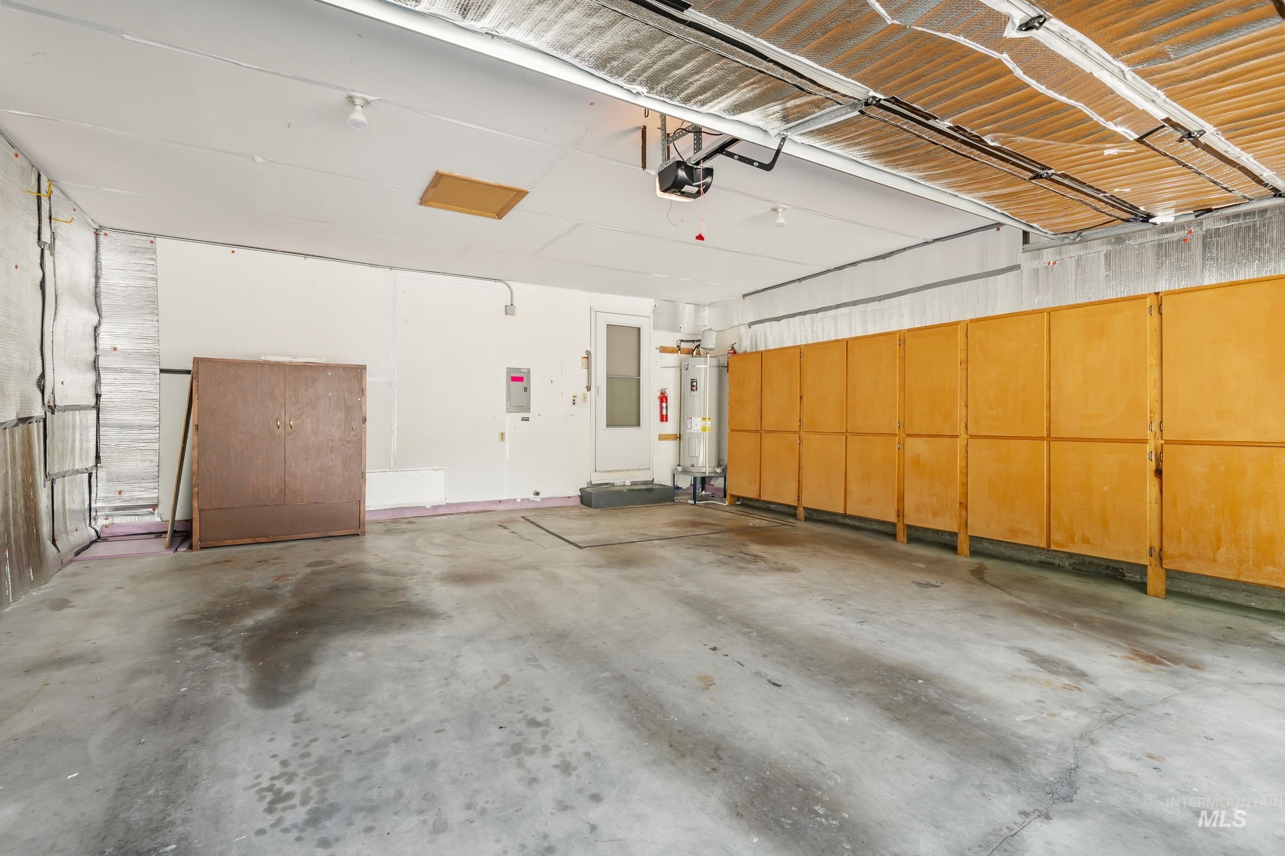 Garage featuring electric water heater, a garage door opener, and electric panel