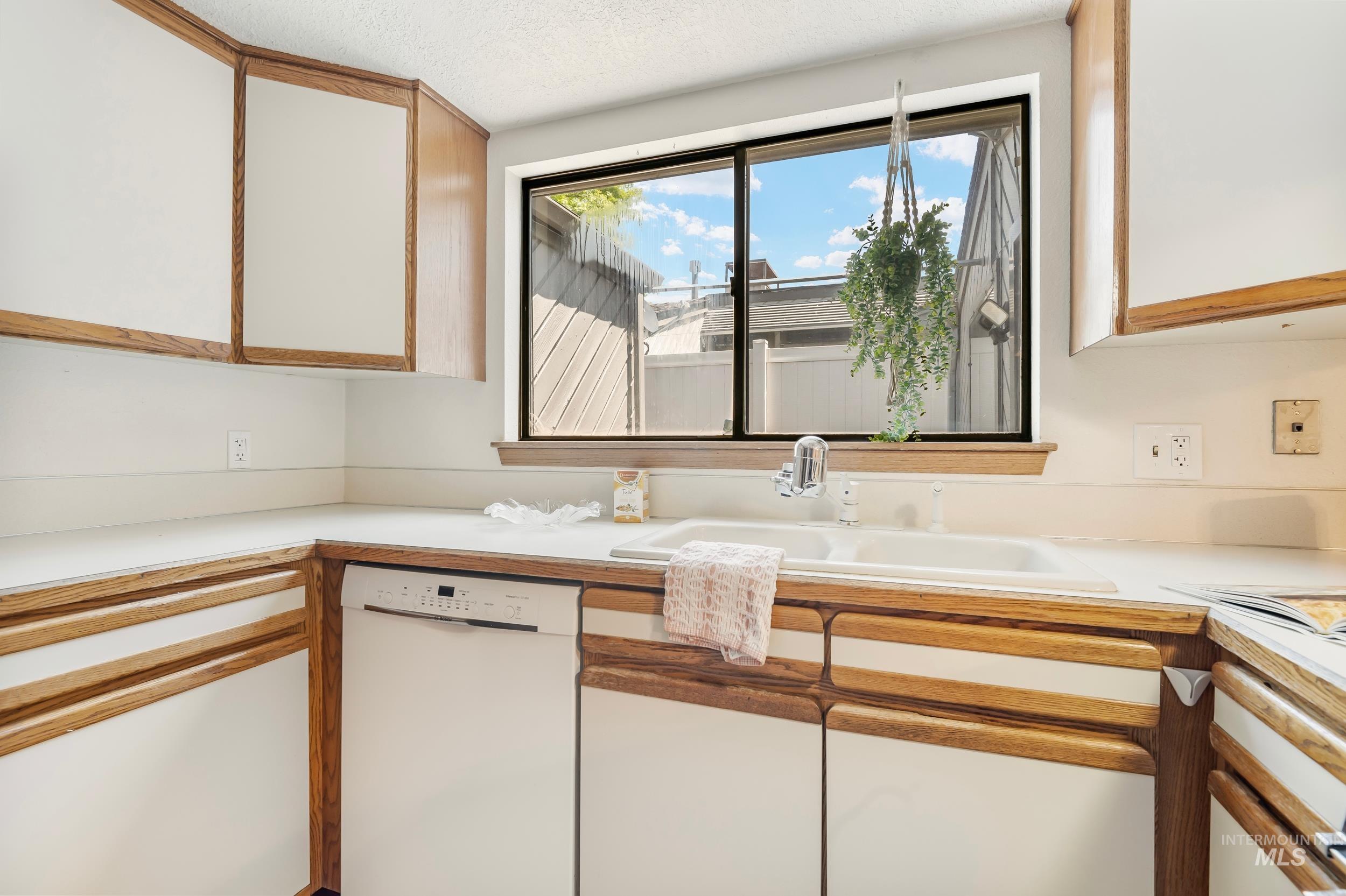 Kitchen featuring dishwasher, white cabinets, light countertops, and a textured ceiling