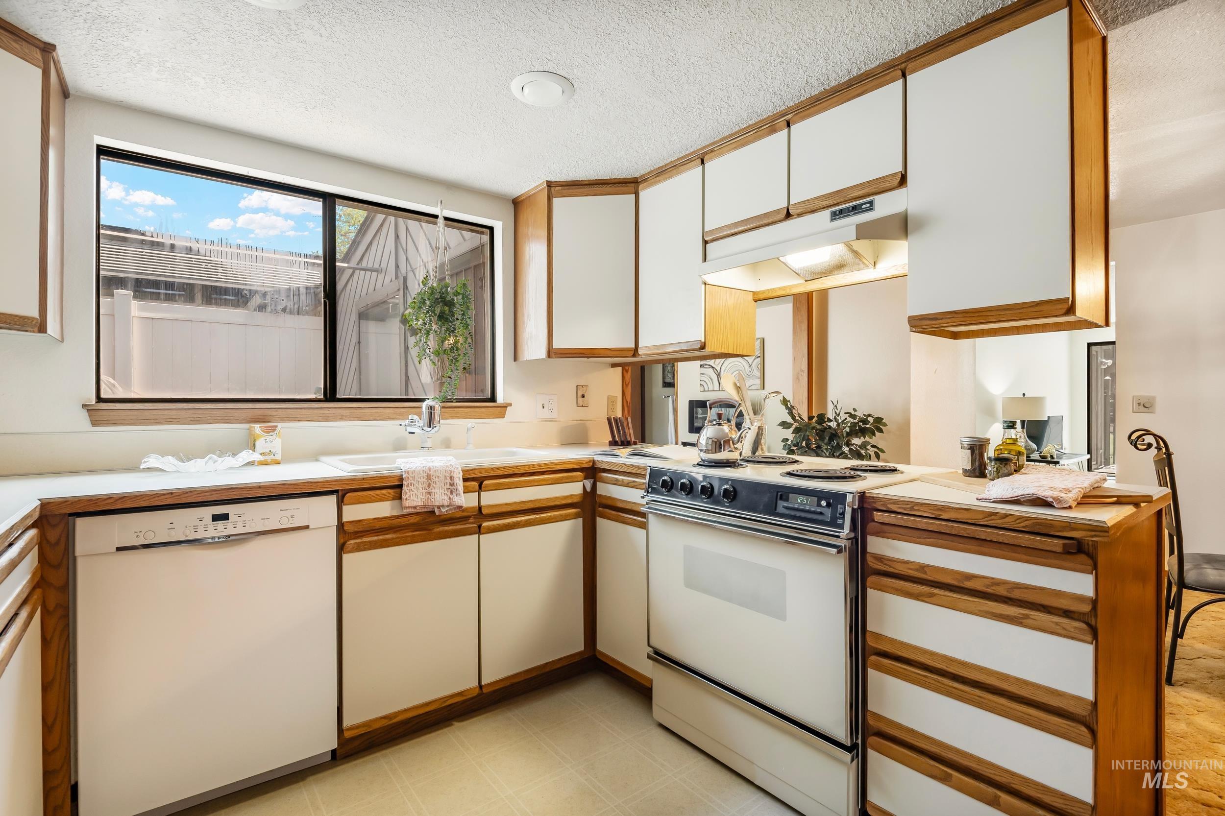 Kitchen featuring white appliances, under cabinet range hood, light countertops, a textured ceiling, and white cabinetry