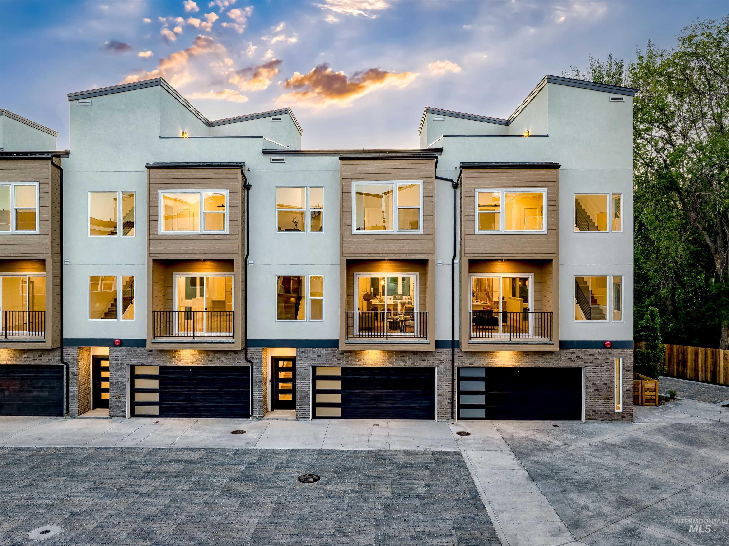 Back of property at dusk featuring a balcony, driveway, an attached garage, and stucco siding
