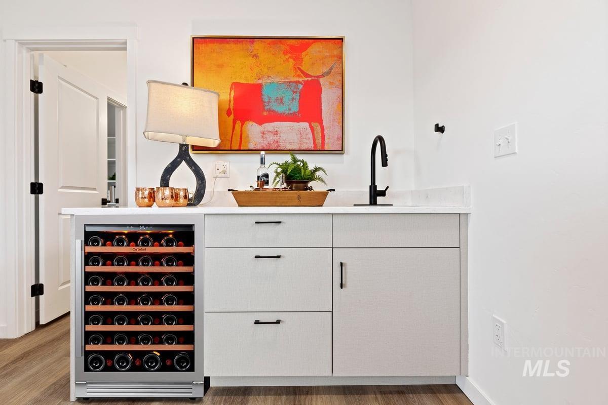 Bar area featuring white cabinetry, beverage cooler, light wood-type flooring, and light stone countertops