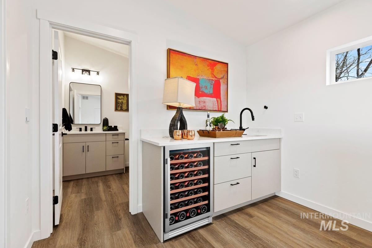 Indoor wet bar featuring white cabinets, beverage cooler, dark wood finished floors, and light stone counters