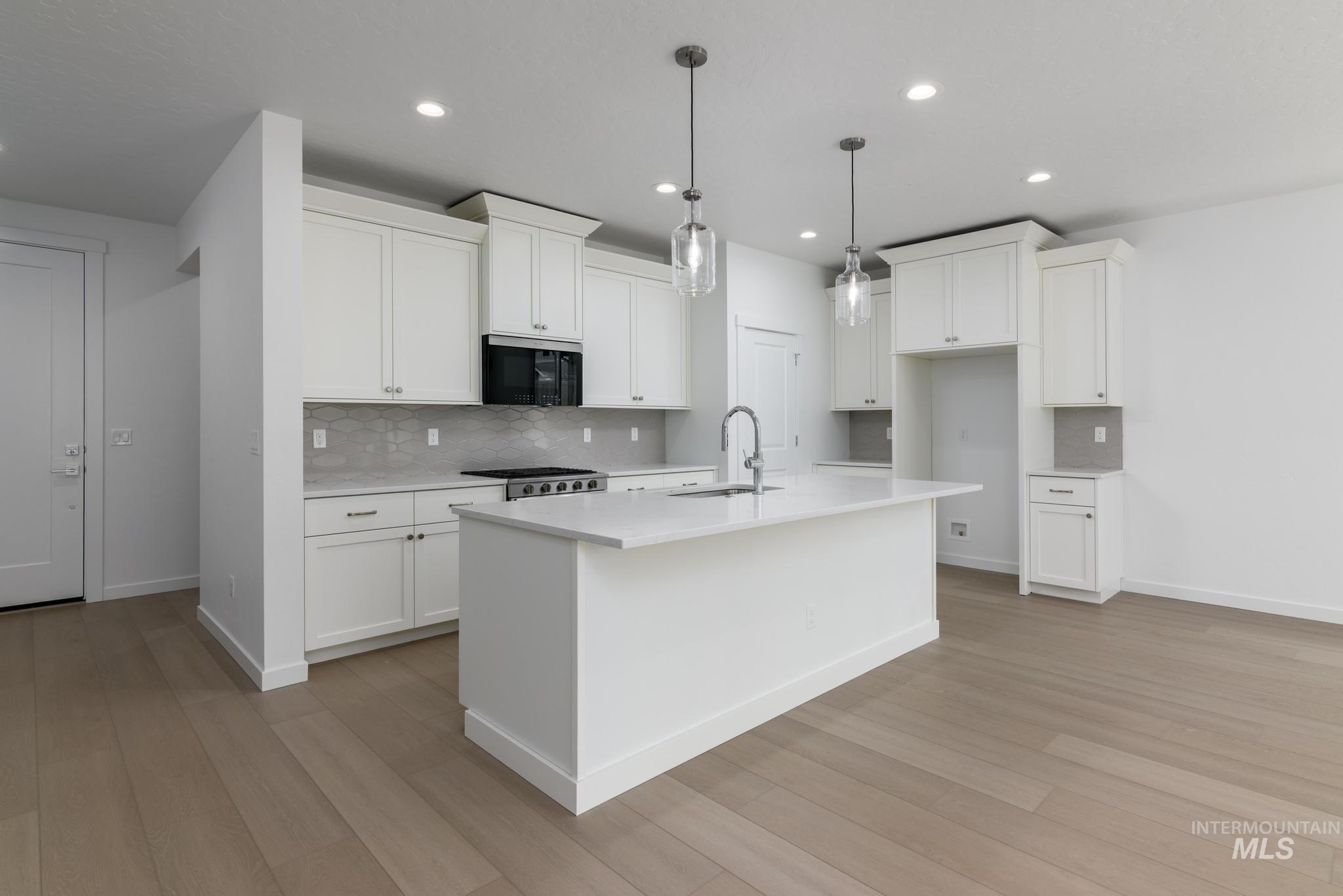 Kitchen featuring appliances with stainless steel finishes, white cabinetry, hanging light fixtures, an island with sink, and backsplash