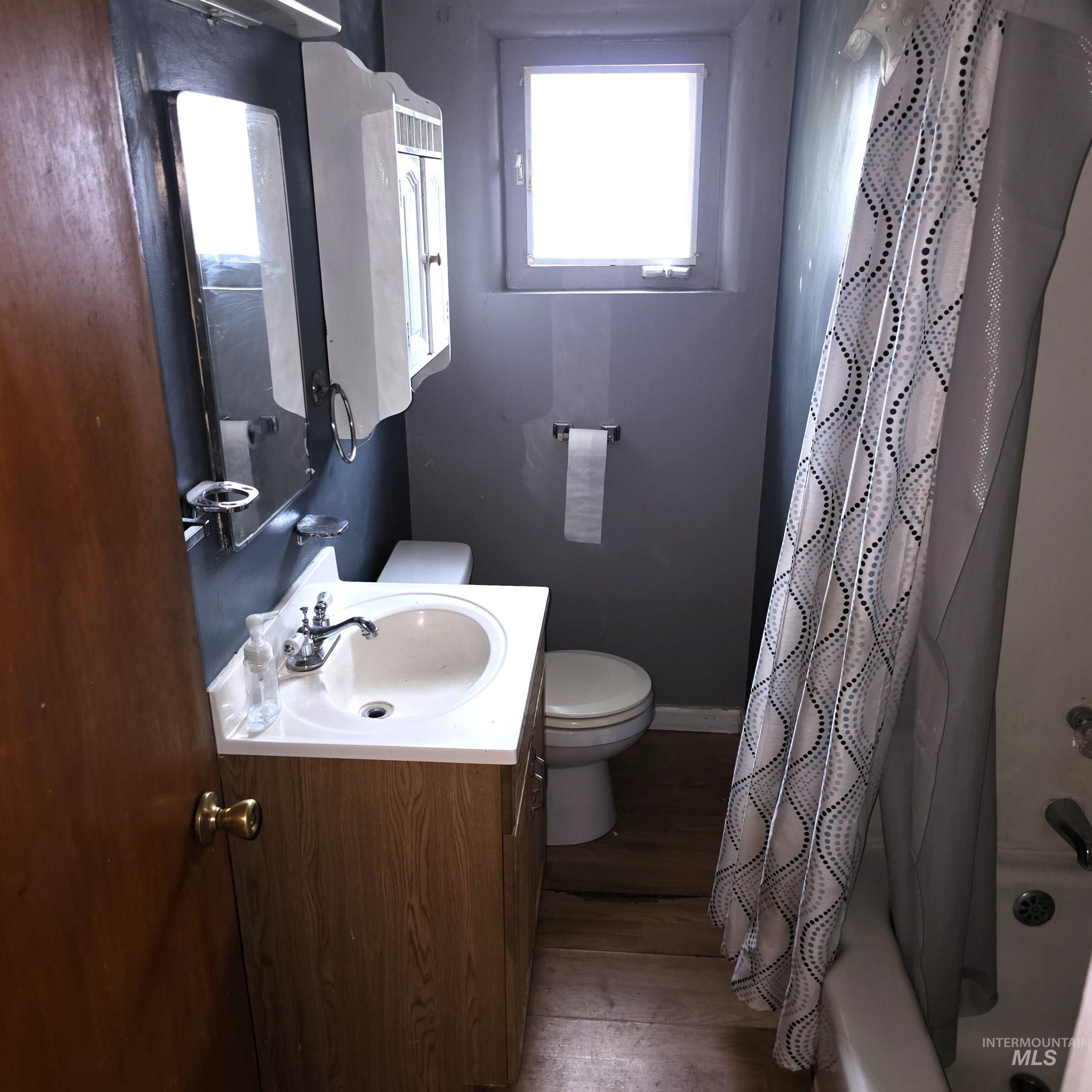 Bathroom with dark wood finished floors, vanity, and shower / tub combo with curtain