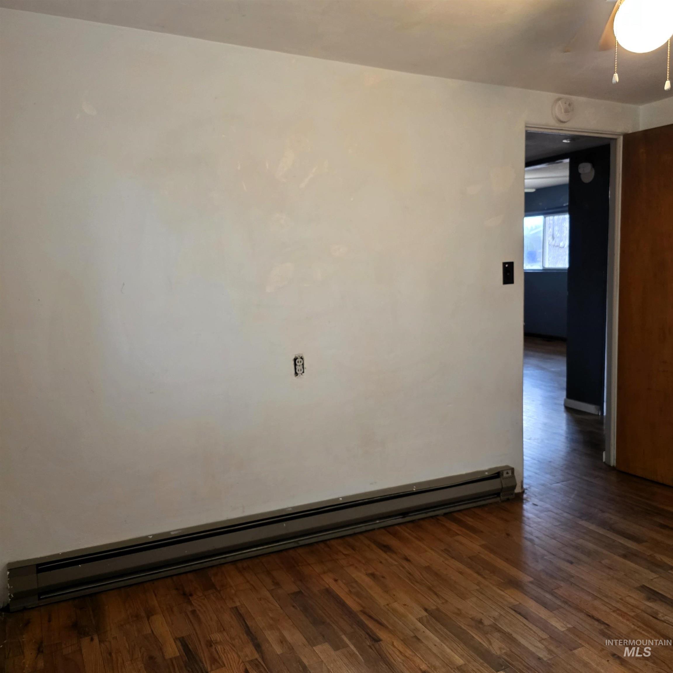 Spare room featuring a baseboard radiator, dark wood-style flooring, and ceiling fan