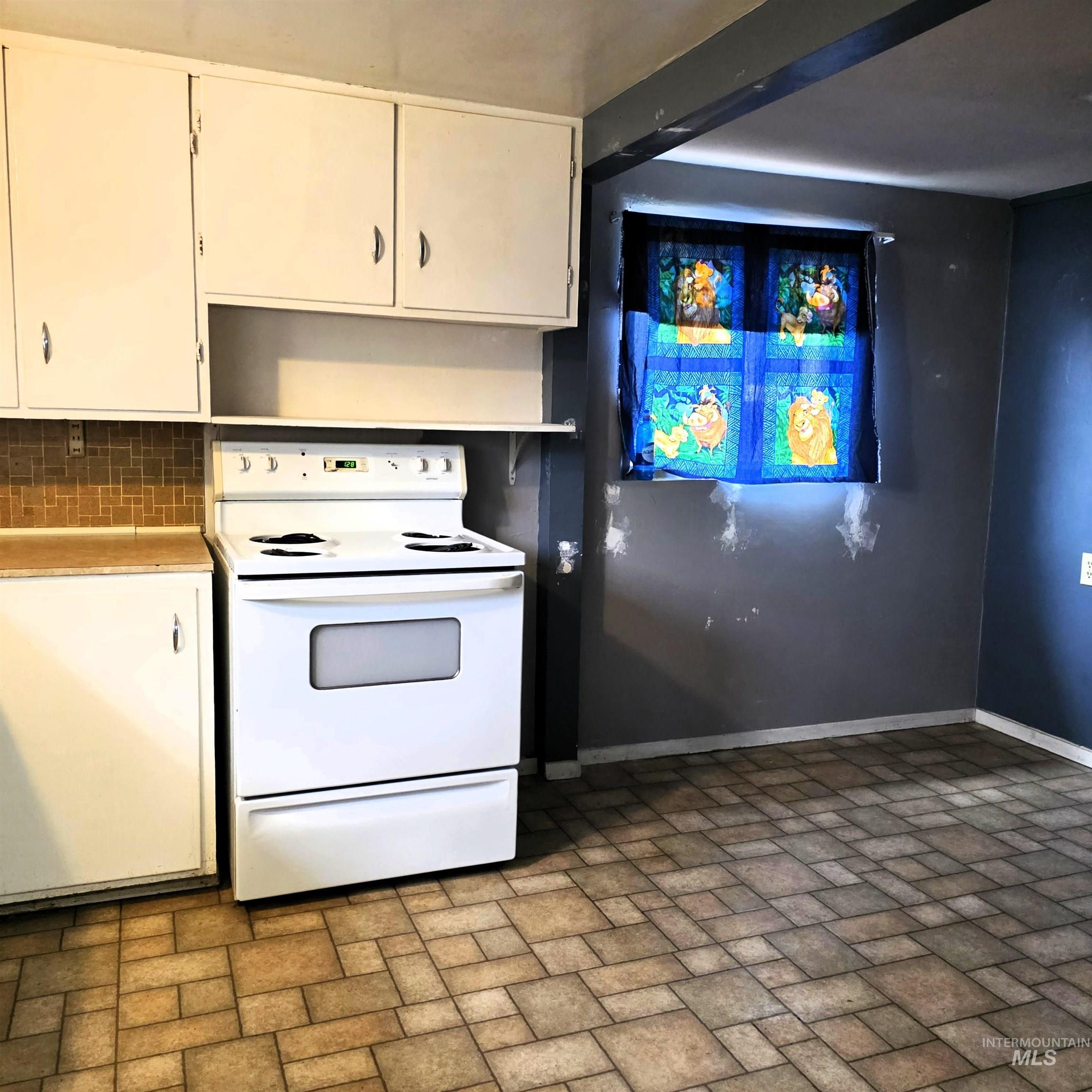 Kitchen featuring electric range, white cabinets, brick patterned flooring, light countertops, and decorative backsplash