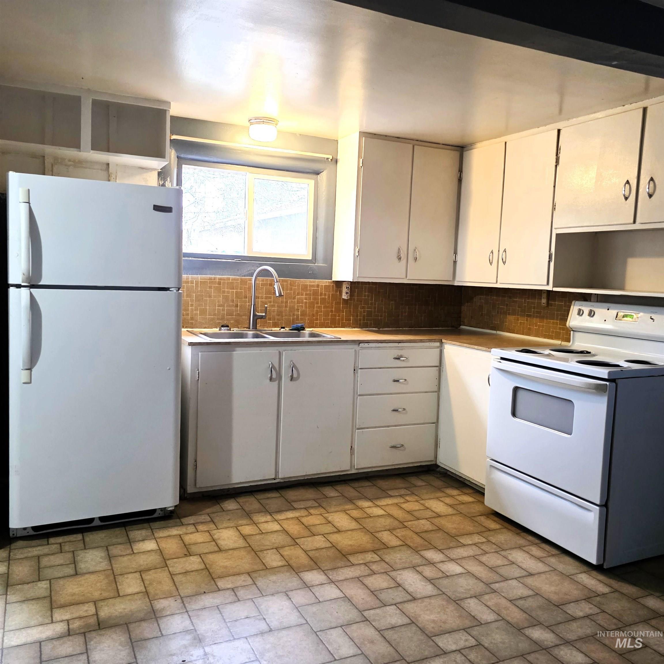 Kitchen featuring white appliances, white cabinets, brick patterned floors, and tasteful backsplash