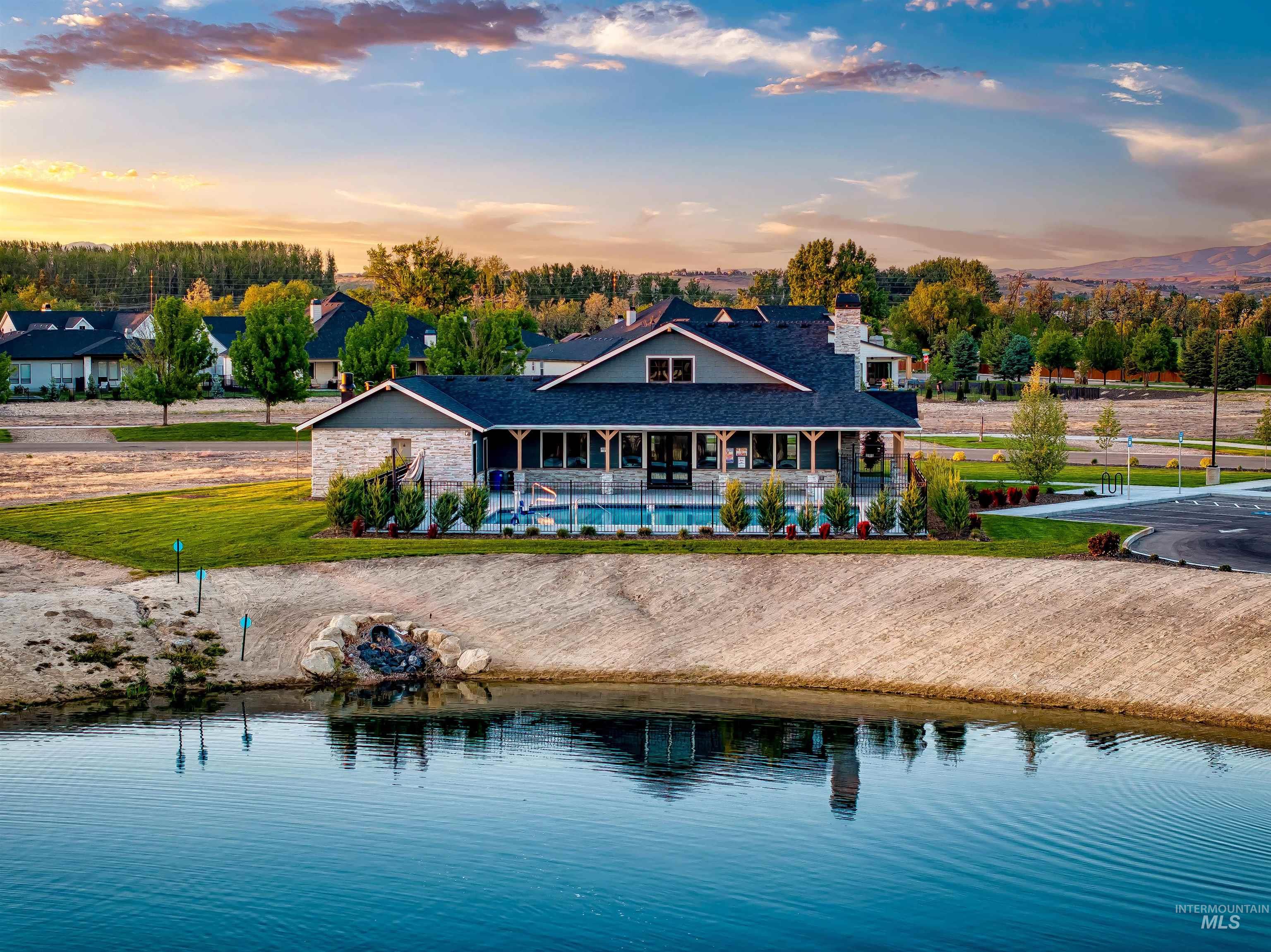 Back of house at dusk with a water view, a patio, a lawn, an outdoor pool, and a chimney