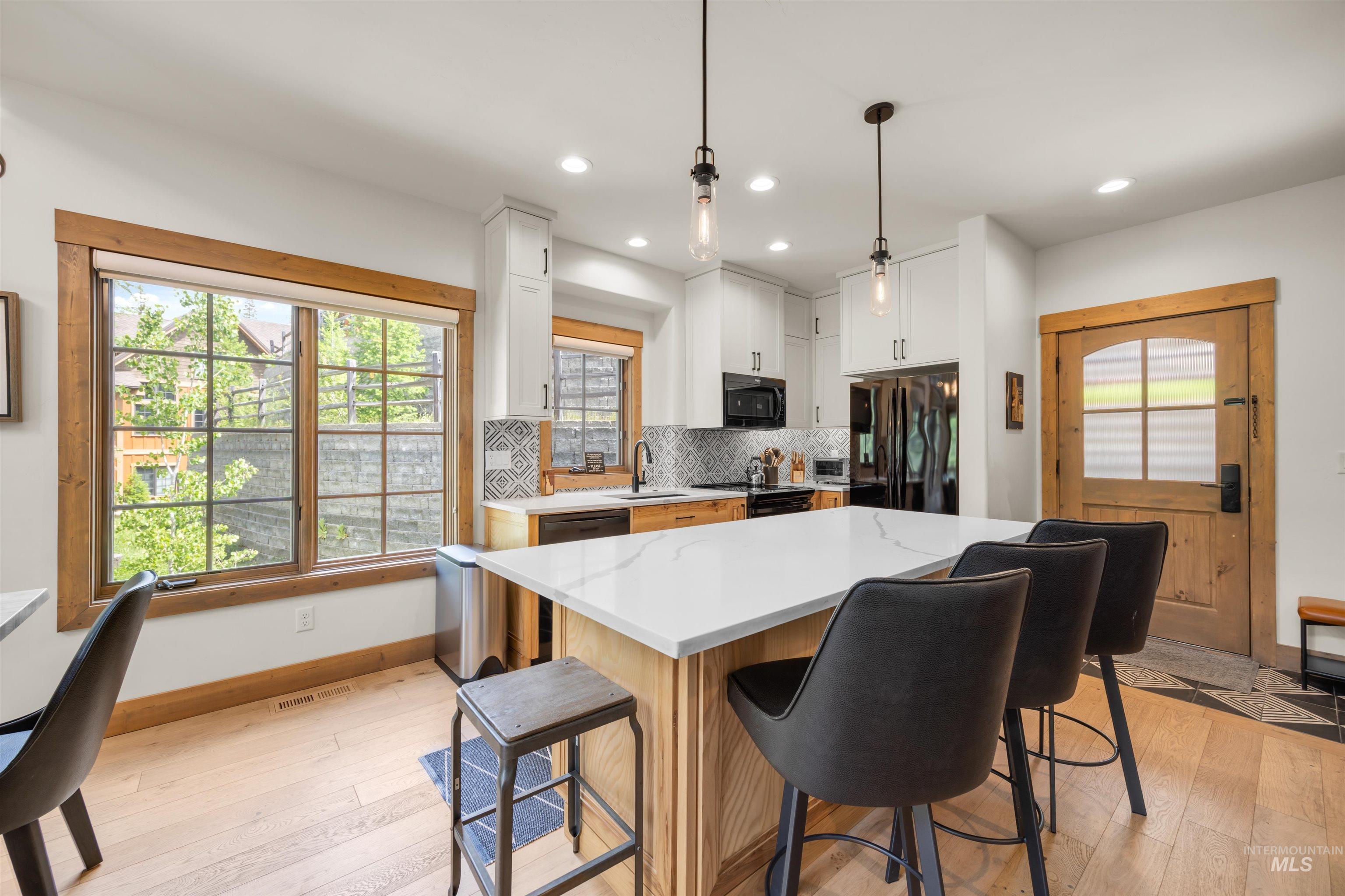 Kitchen featuring a large island with a light-toned countertop, pendant lighting, white cabinetry, dark appliances, and a patterned backsplash