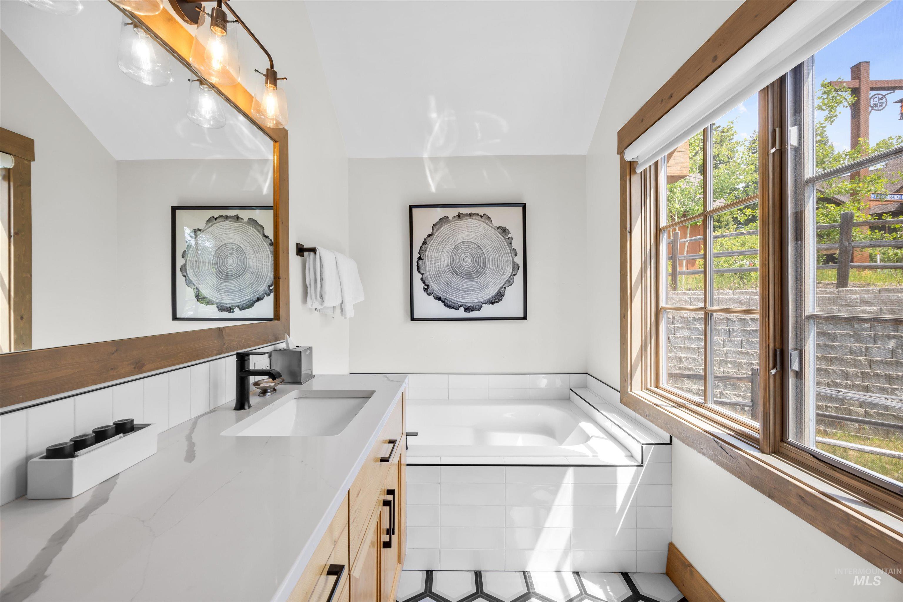 Bathroom featuring a built-in soaking tub, a large multi-pane window with wood-finish trim, and a vanity with an integrated sink and quartz countertop