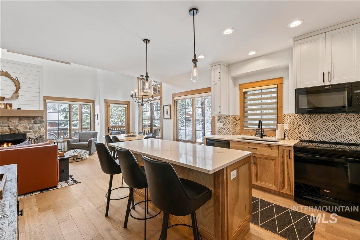 Two tone kitchen with black appliances, open floor plan, dual tone cabinetry, a center island, and light wood-type flooring