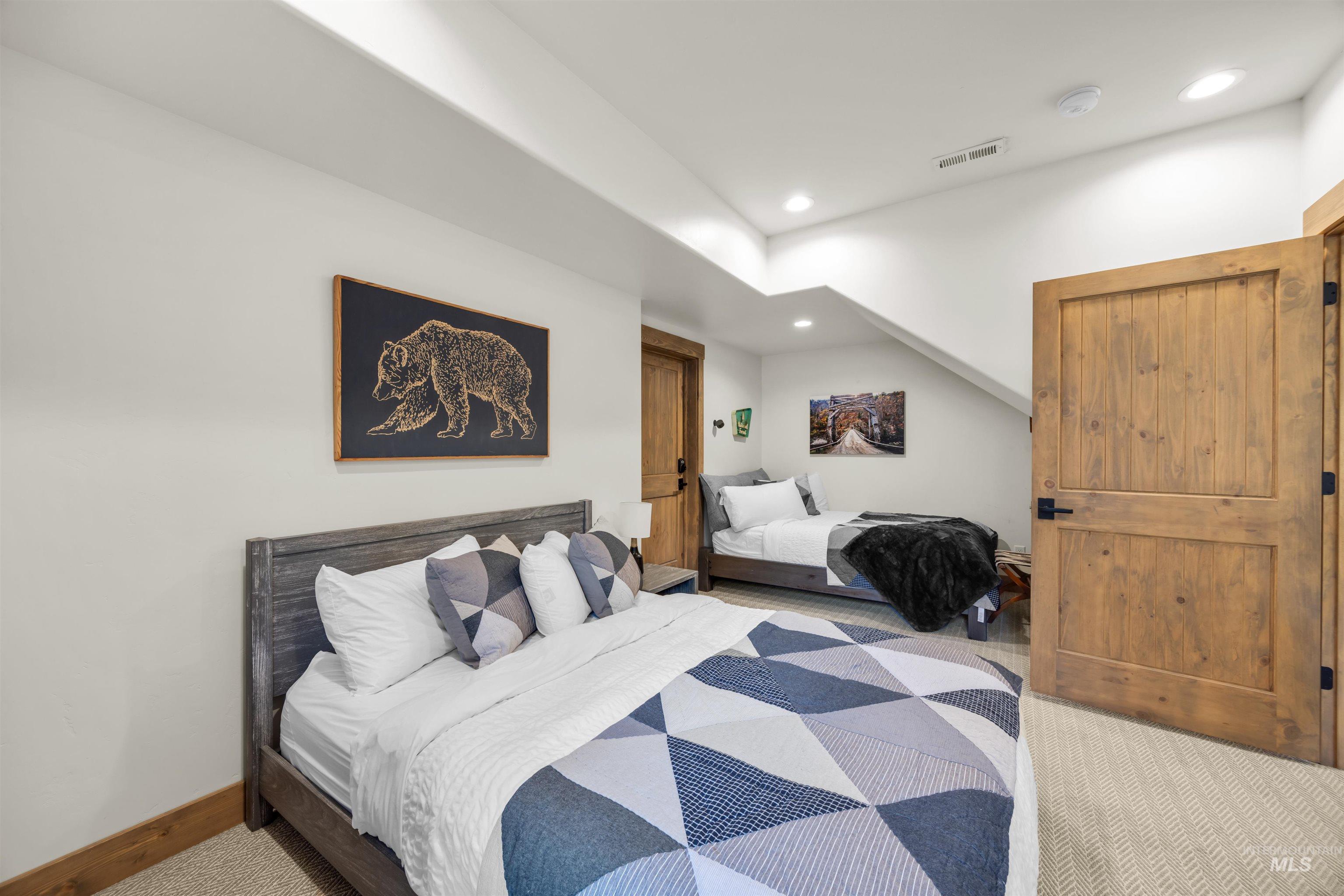 Spacious room featuring light-toned walls, recessed lighting, natural wood doors with black hardware, and textured carpeting