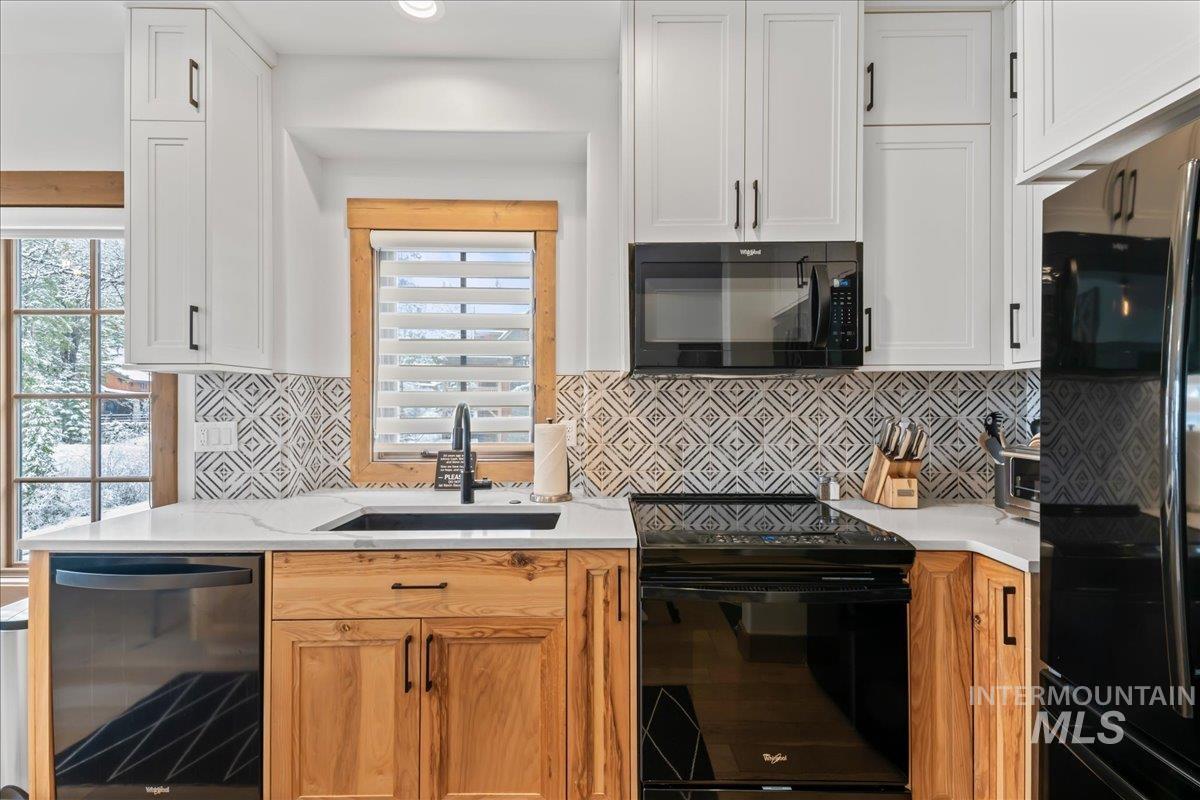Kitchen with black appliances, white cabinets, and light stone countertops