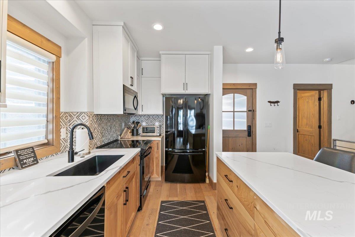 Two tone kitchen with light wood finished floors, black appliances, pendant lighting, two tone cabinetry, and light stone countertops