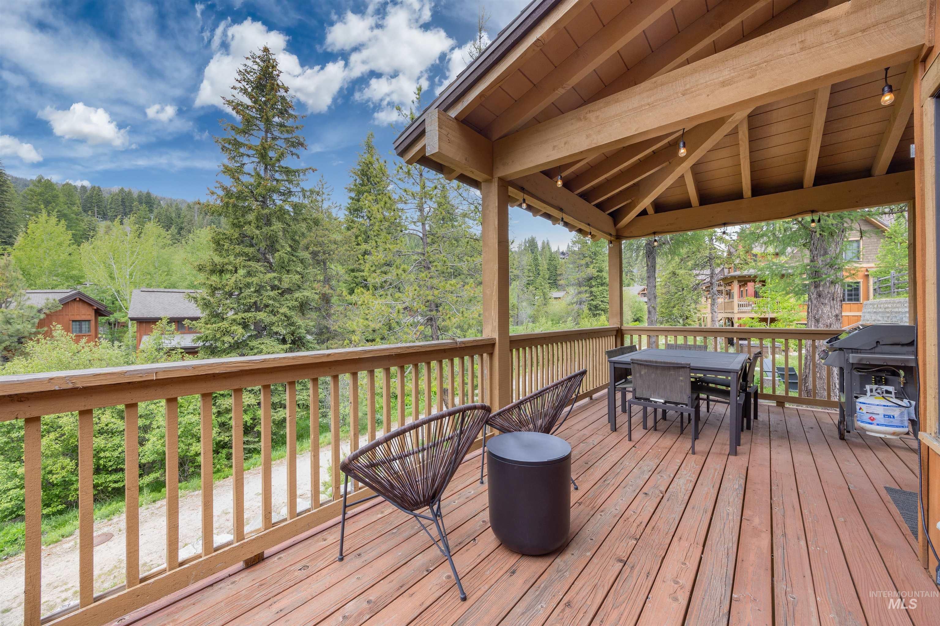 Expansive wood-finish deck featuring a covered area with exposed beam ceiling, string lighting, and wood railing