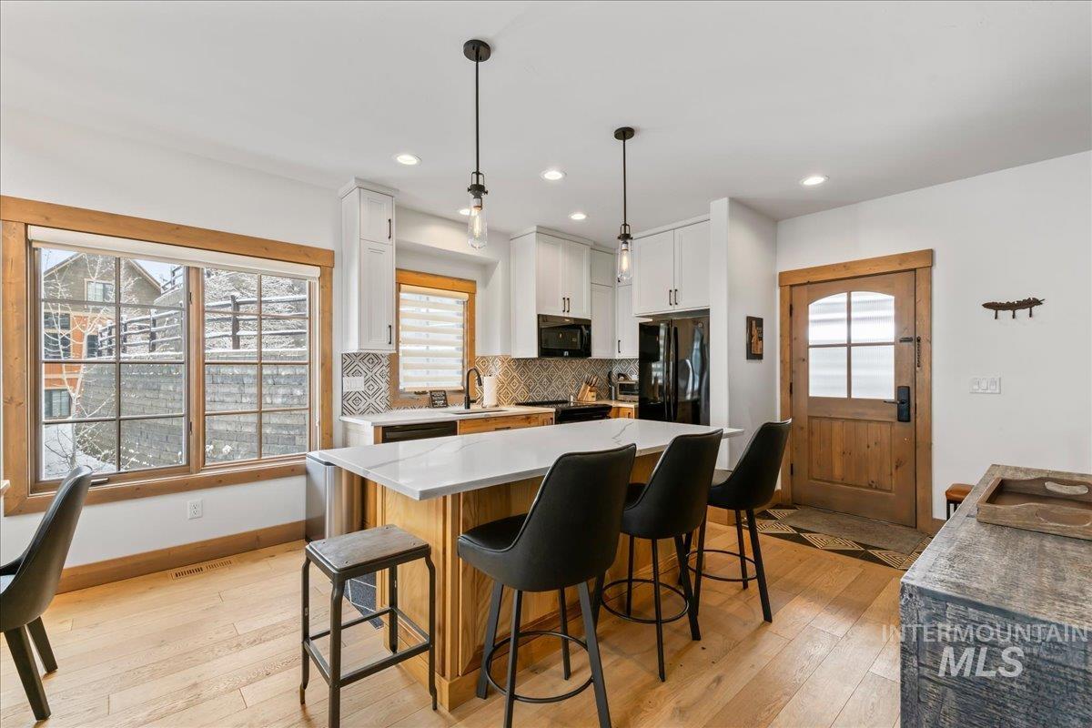 Kitchen featuring light wood finished floors, a center island, light stone countertops, plenty of natural light, and two tone cabinetry