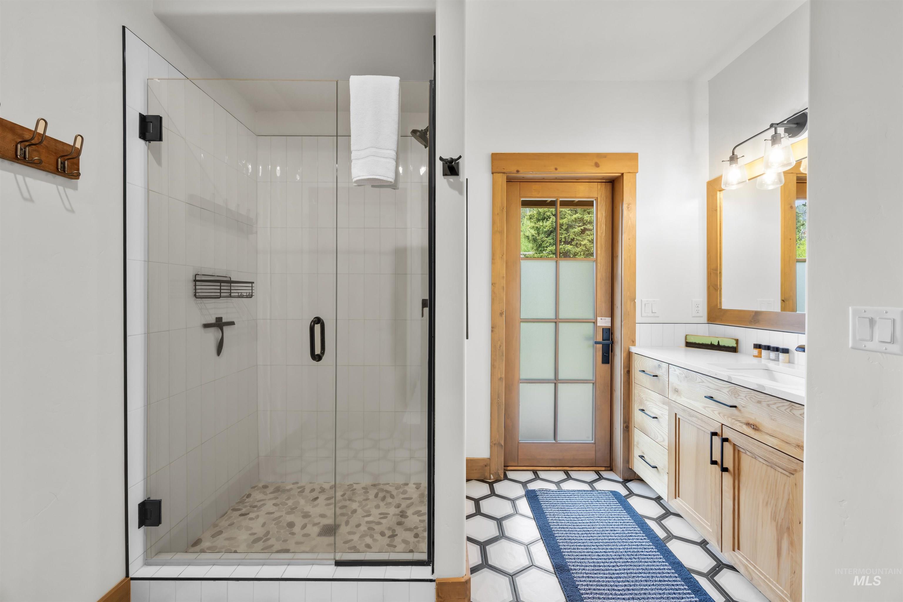 Bathroom featuring a glass-enclosed shower with pebble-tile flooring, a wood-finish vanity with countertop, and hex-pattern floor tiling