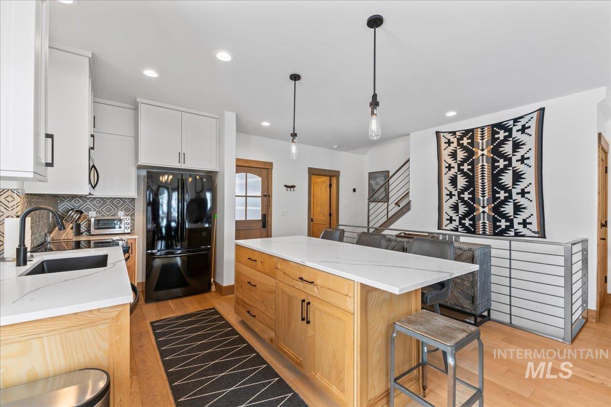 Two tone kitchen with freestanding refrigerator, a center island, light stone counters, light wood-type flooring, and two tone color scheme