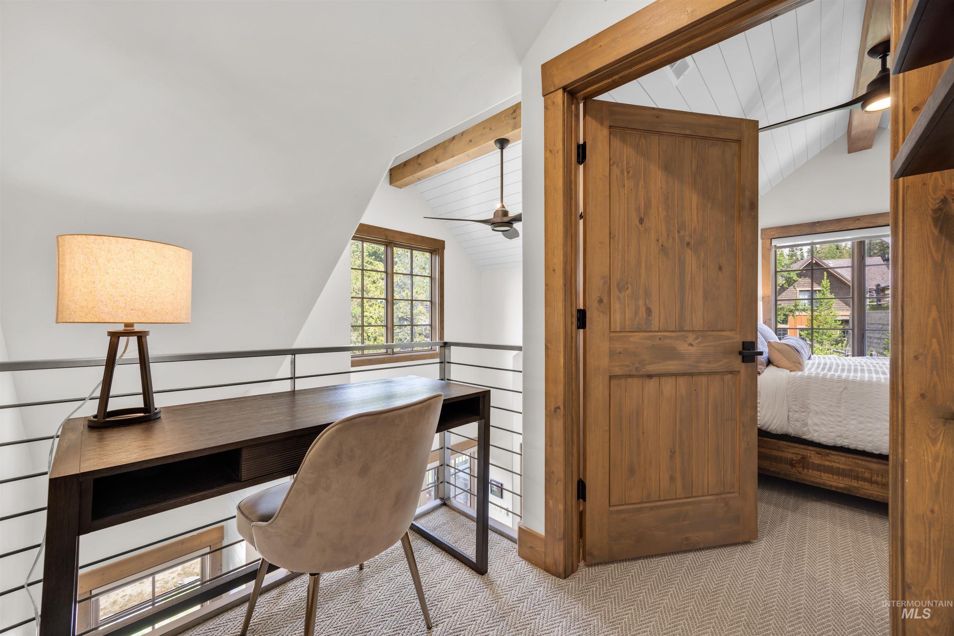 Loft area featuring a wood-finish desk, metal balustrade railing, and herringbone carpet flooring