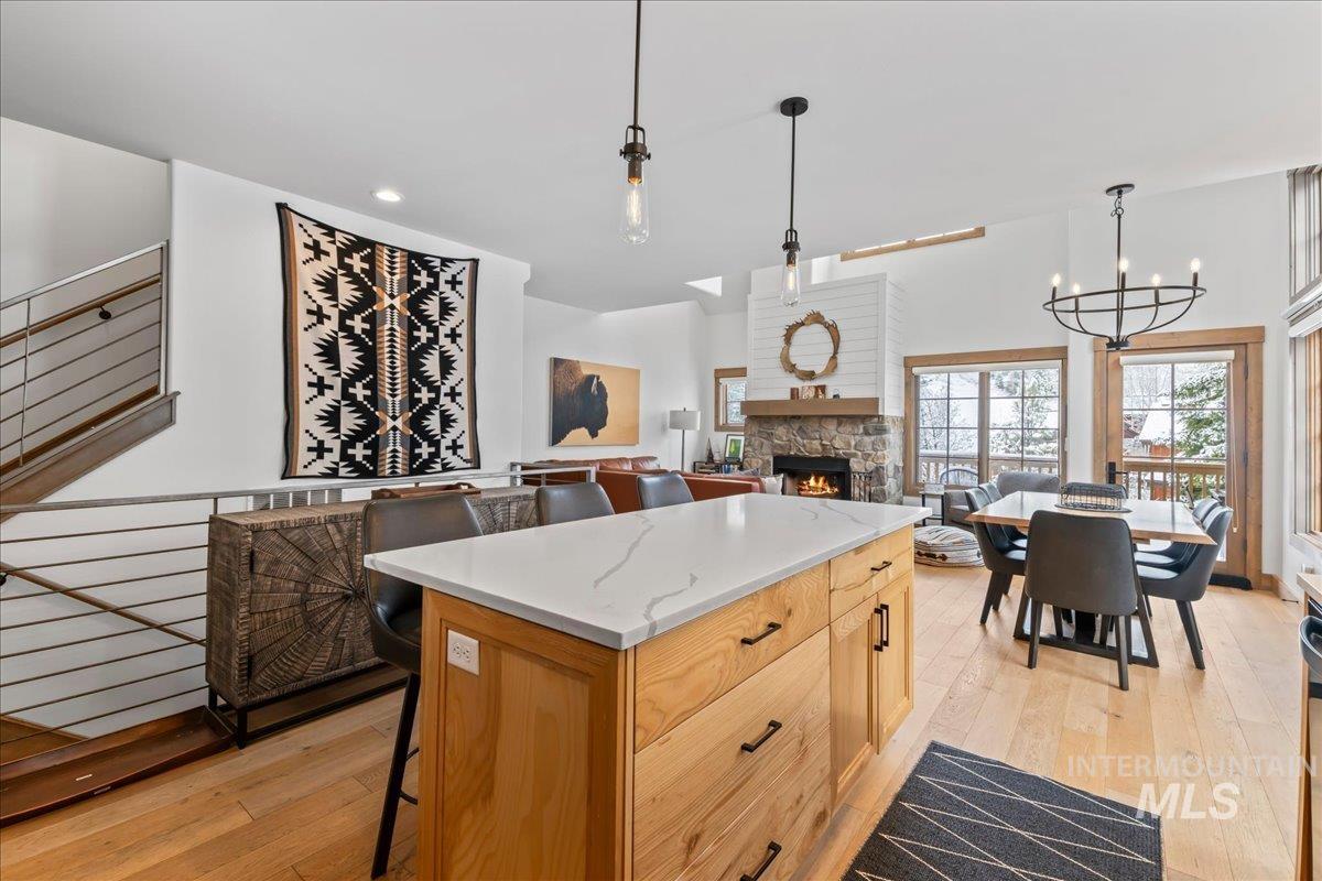 Kitchen with a breakfast bar, light wood-type flooring, a center island, a fireplace, and light stone countertops