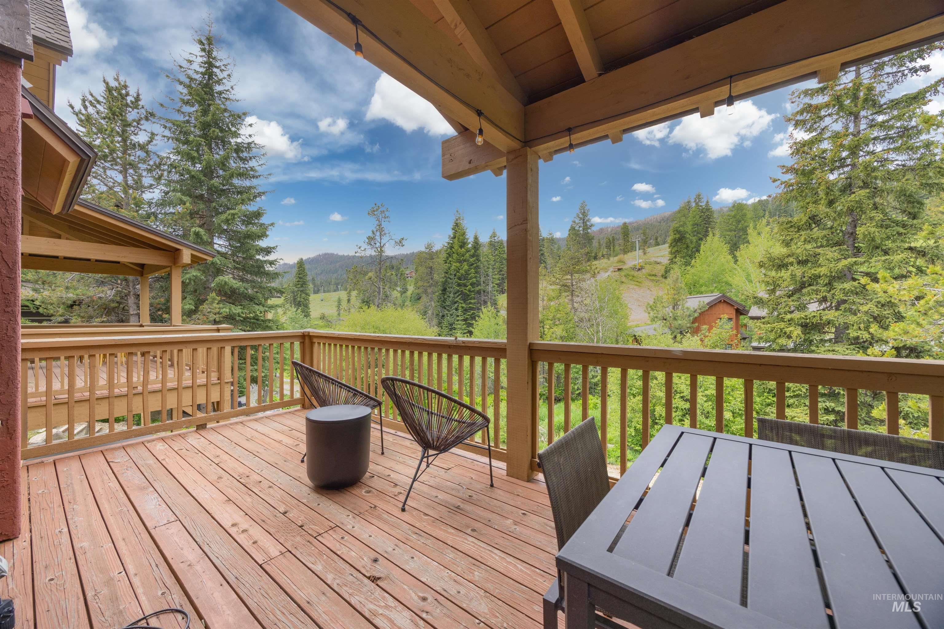 Expansive wood-finish deck with natural wood railings, exposed wood beam ceiling, and a prominent mountain backdrop with mature evergreen trees