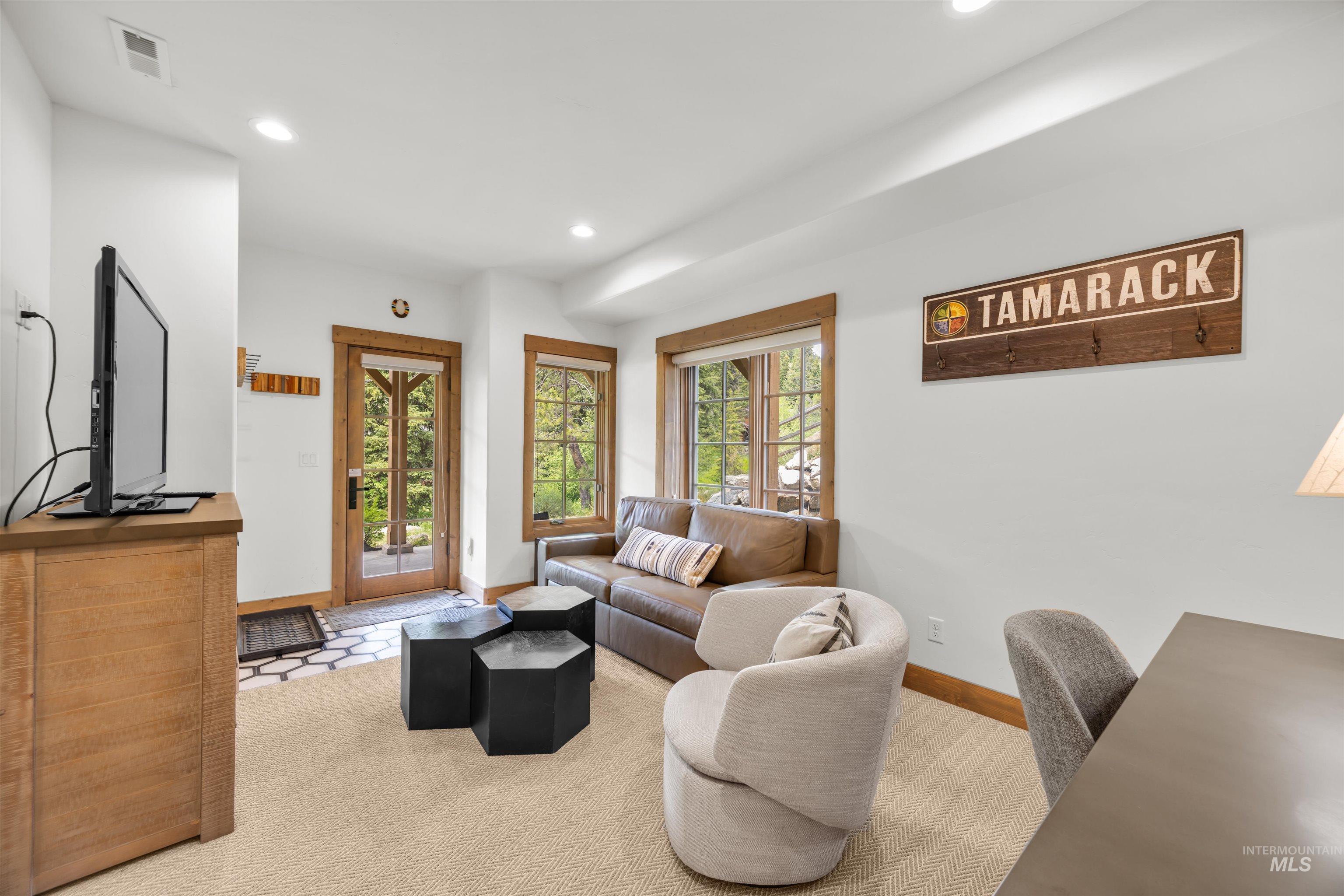 Light-filled living area featuring a glass-paned entry door, wood-trimmed windows, recessed lighting, and soft carpeting
