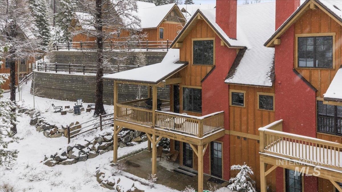 Snow covered back of property featuring a chimney, board and batten siding, a patio area, and a wooden deck