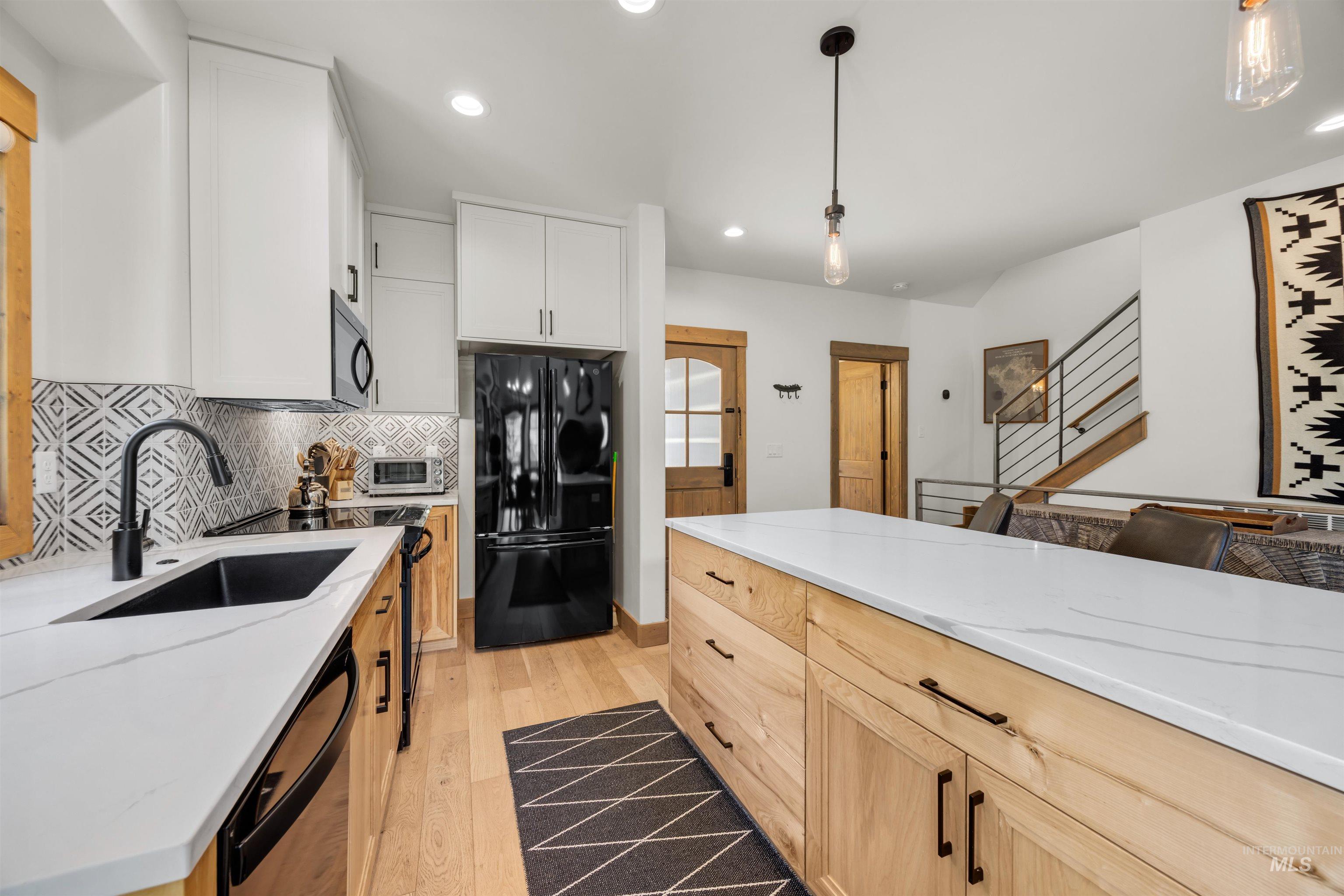 Kitchen featuring an integrated black sink, white countertops, mixed material cabinetry, black refrigerator, and a patterned backsplash