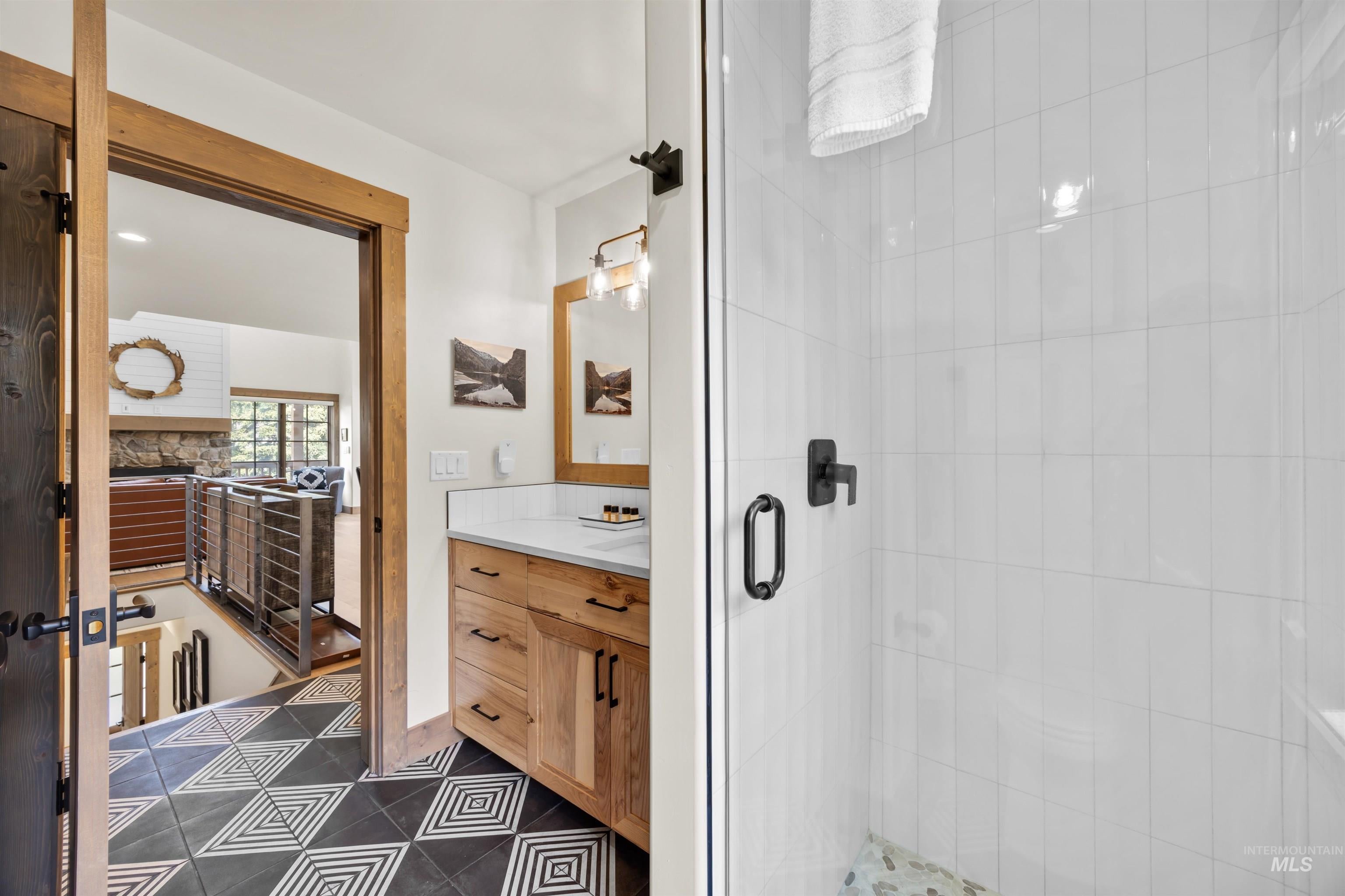 Bathroom featuring a wood vanity with a white countertop, a shower with a clear glass enclosure, white rectangular tile, and a geometric pattern tile floor