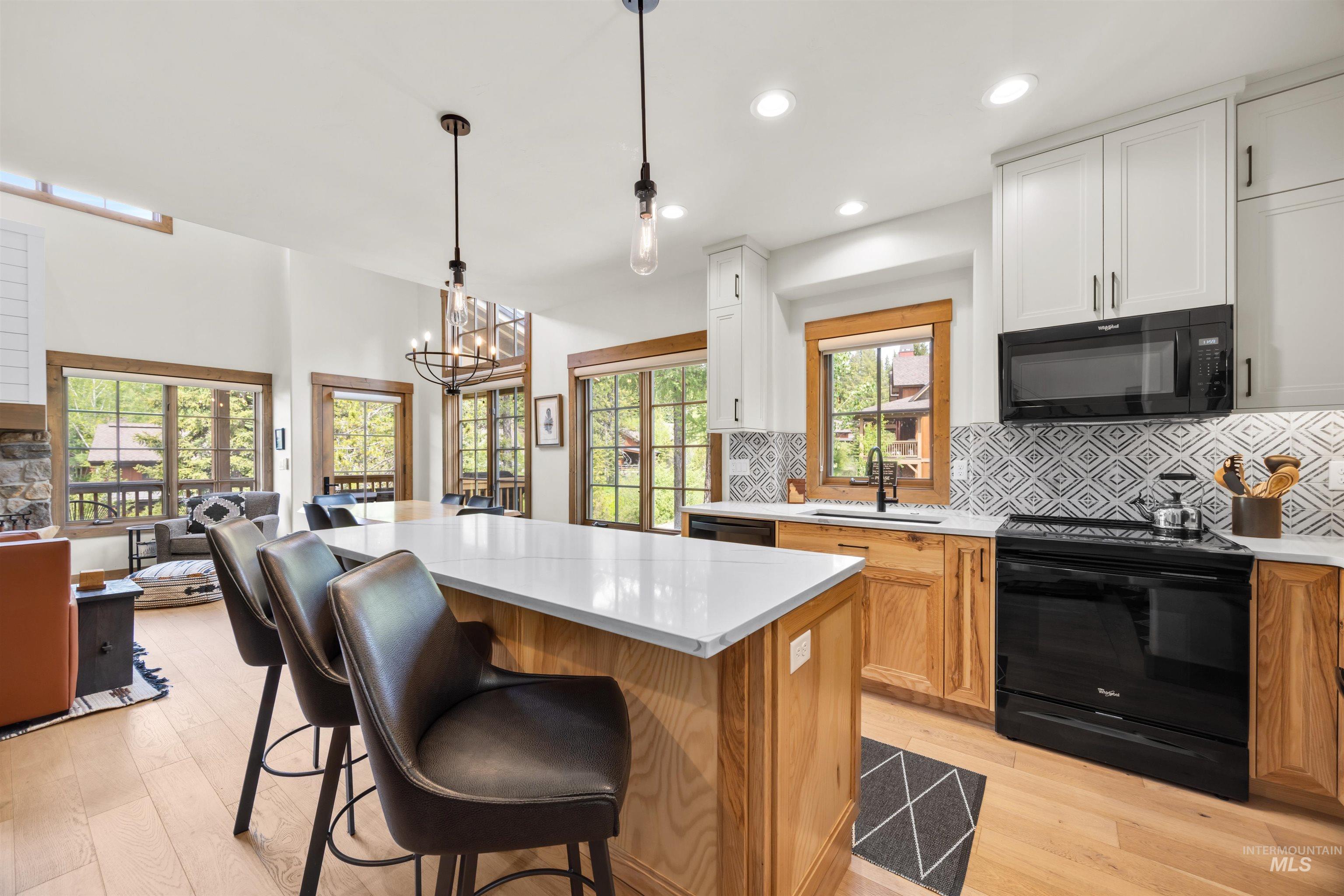Open-concept kitchen featuring an expansive island with a quartz countertop, black appliances, and a patterned tile backsplash