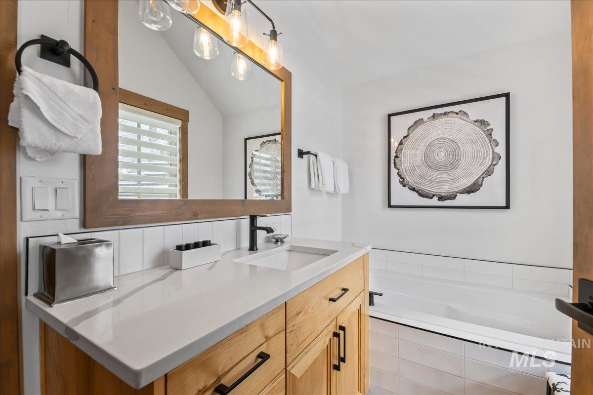 Full bath featuring a bath, vanity, and vaulted ceiling