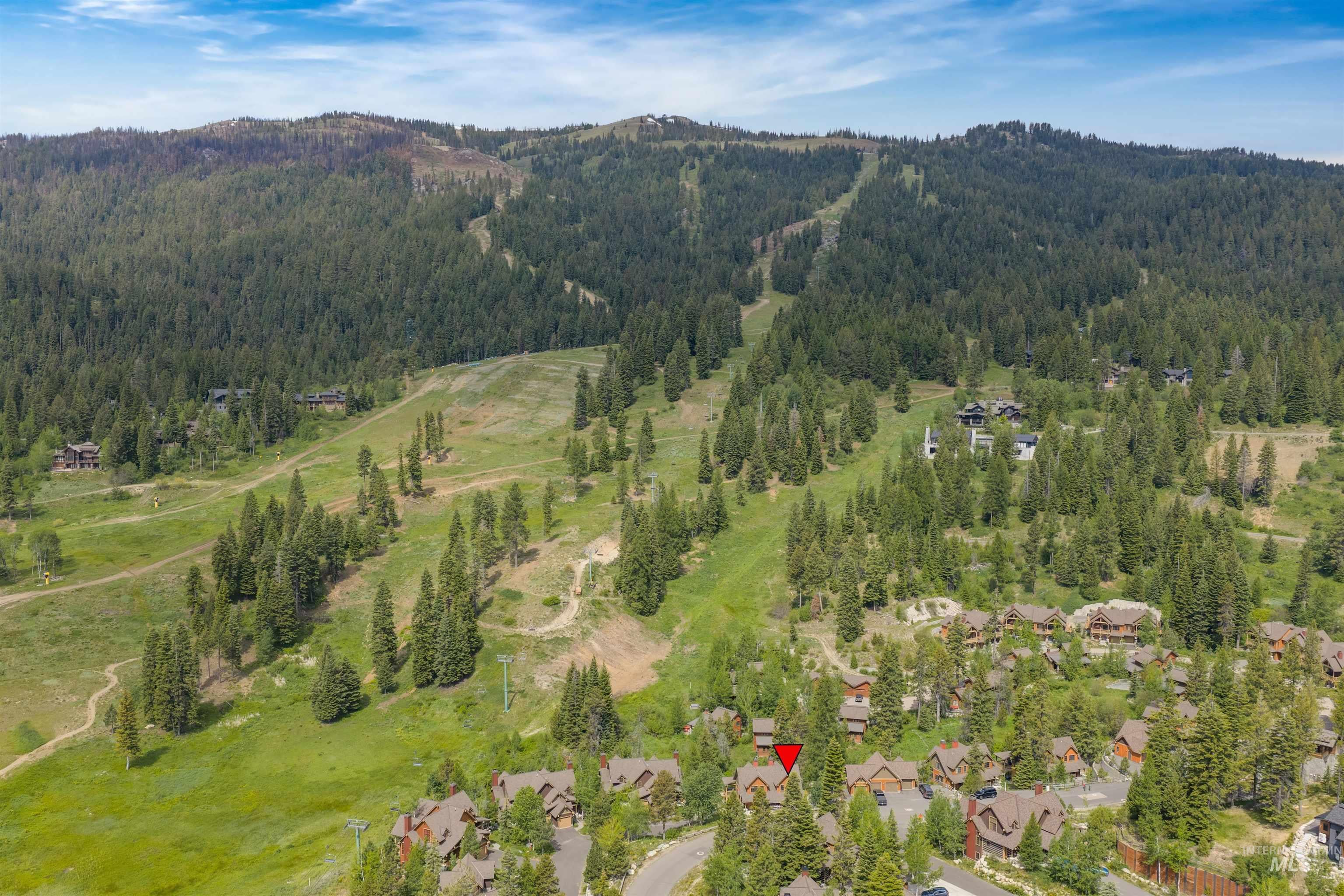 Mountain landscape featuring a residential area with multiple structures, expansive green spaces, and dense tree coverage
