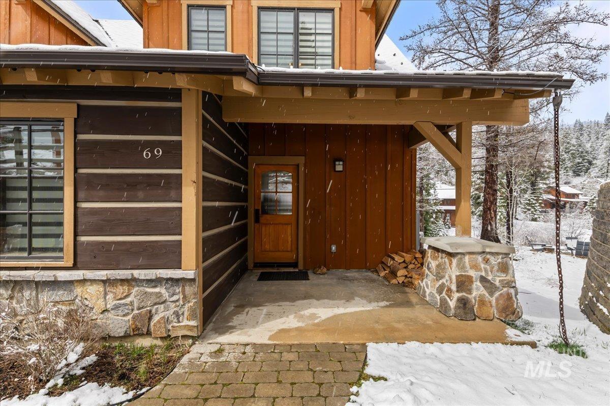 Snow covered property entrance featuring board and batten siding and covered porch