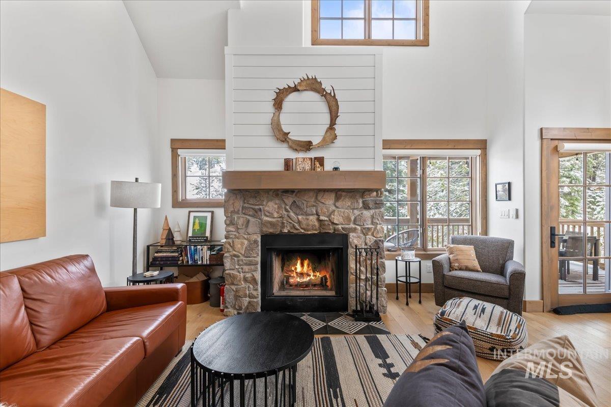 Living area with a high ceiling, light wood finished floors, and a stone fireplace