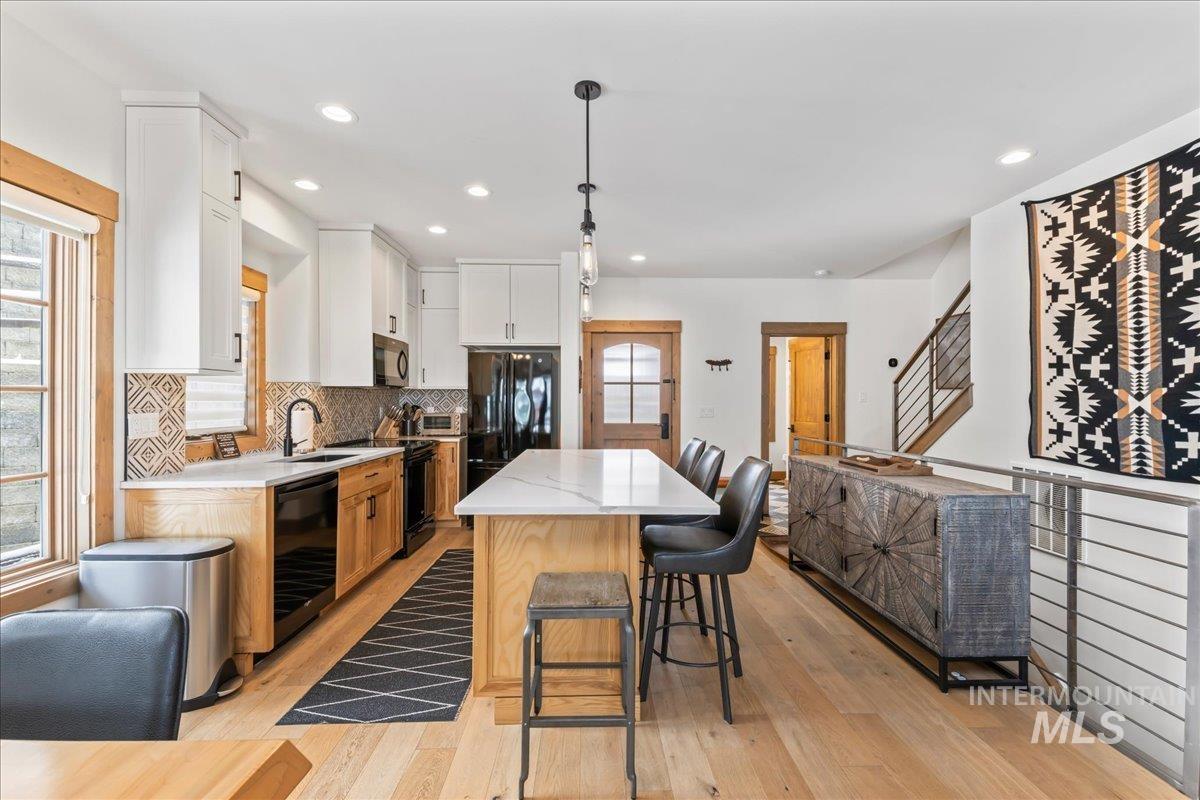 Kitchen with tasteful backsplash, a breakfast bar, light wood-style flooring, two tone cabinetry, and black appliances
