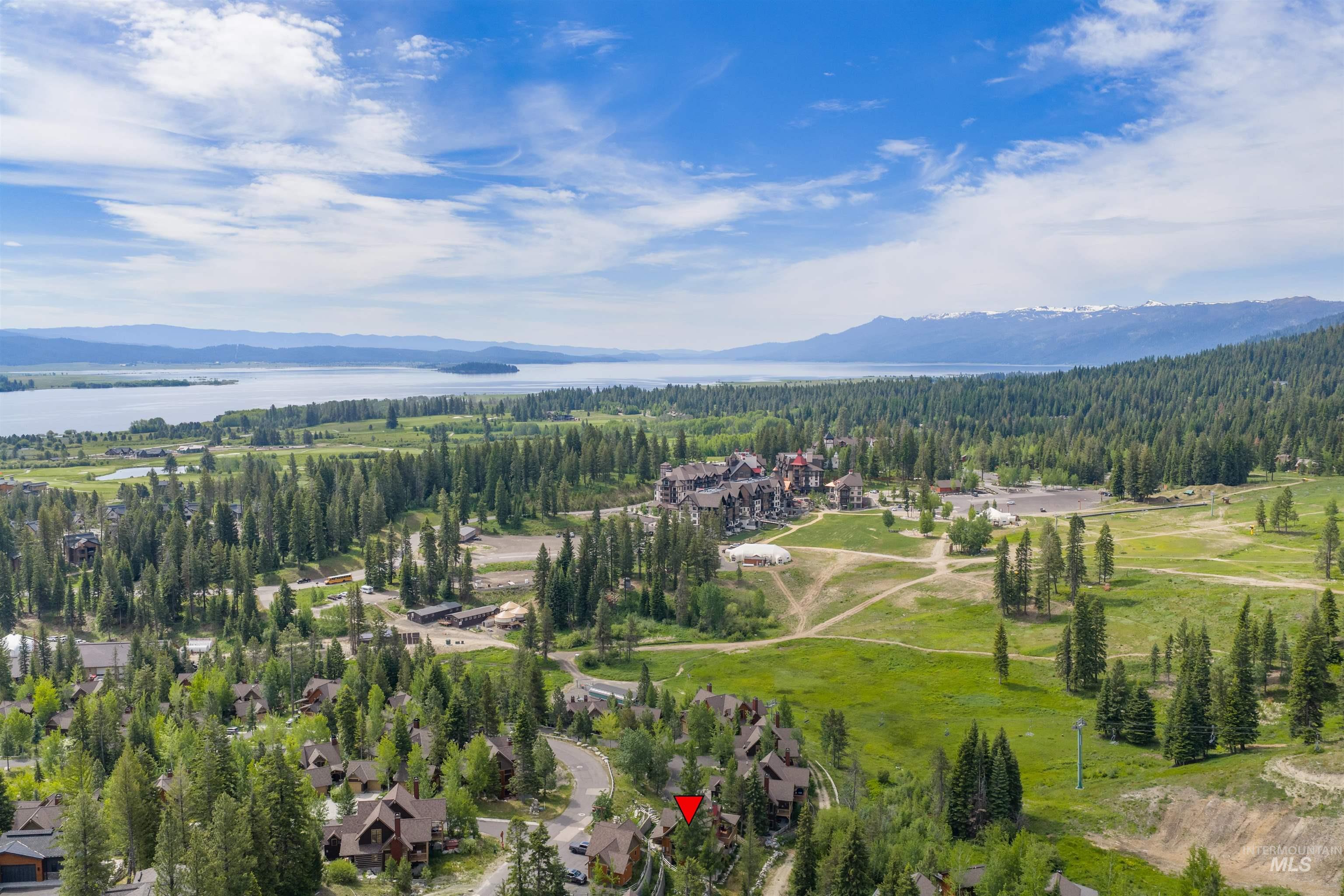 Expansive aerial showcasing a mountainous landscape with a large body of water, dense evergreen forests, and a clustered residential development