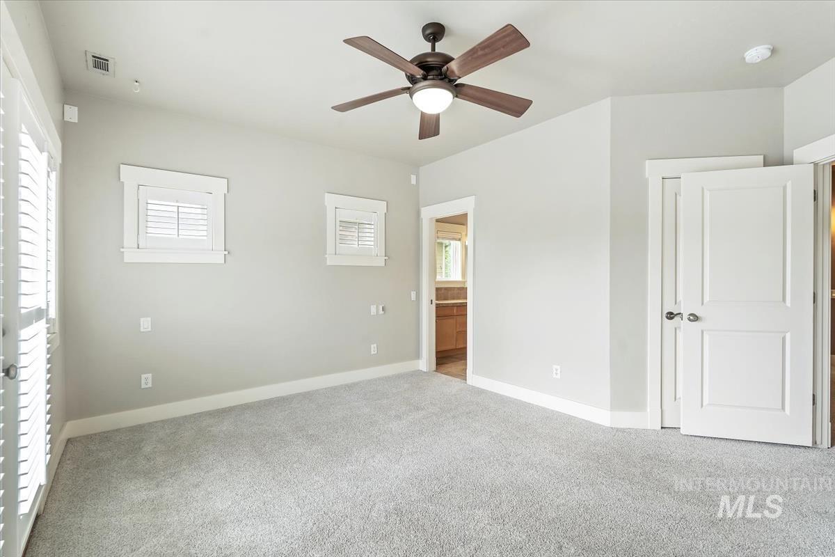 Unfurnished bedroom featuring multiple windows, ensuite bathroom, carpet, and a ceiling fan