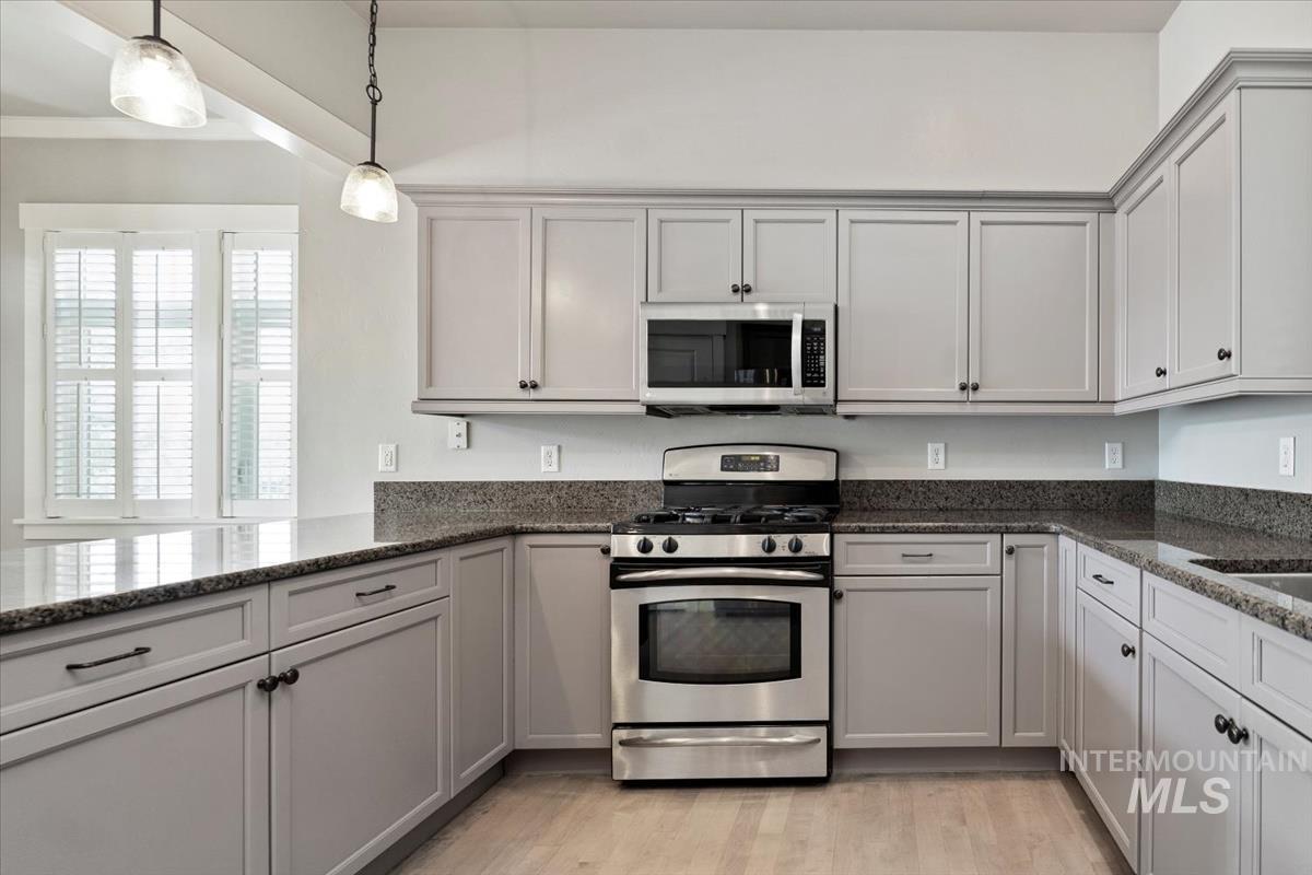 Kitchen with stainless steel appliances, dark stone countertops, light wood-type flooring, pendant lighting, and gray cabinetry