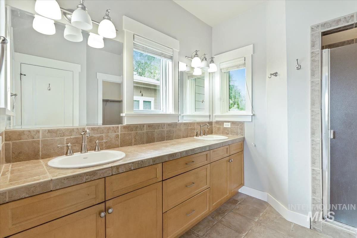 Full bath with a stall shower, double vanity, decorative backsplash, and light tile patterned floors