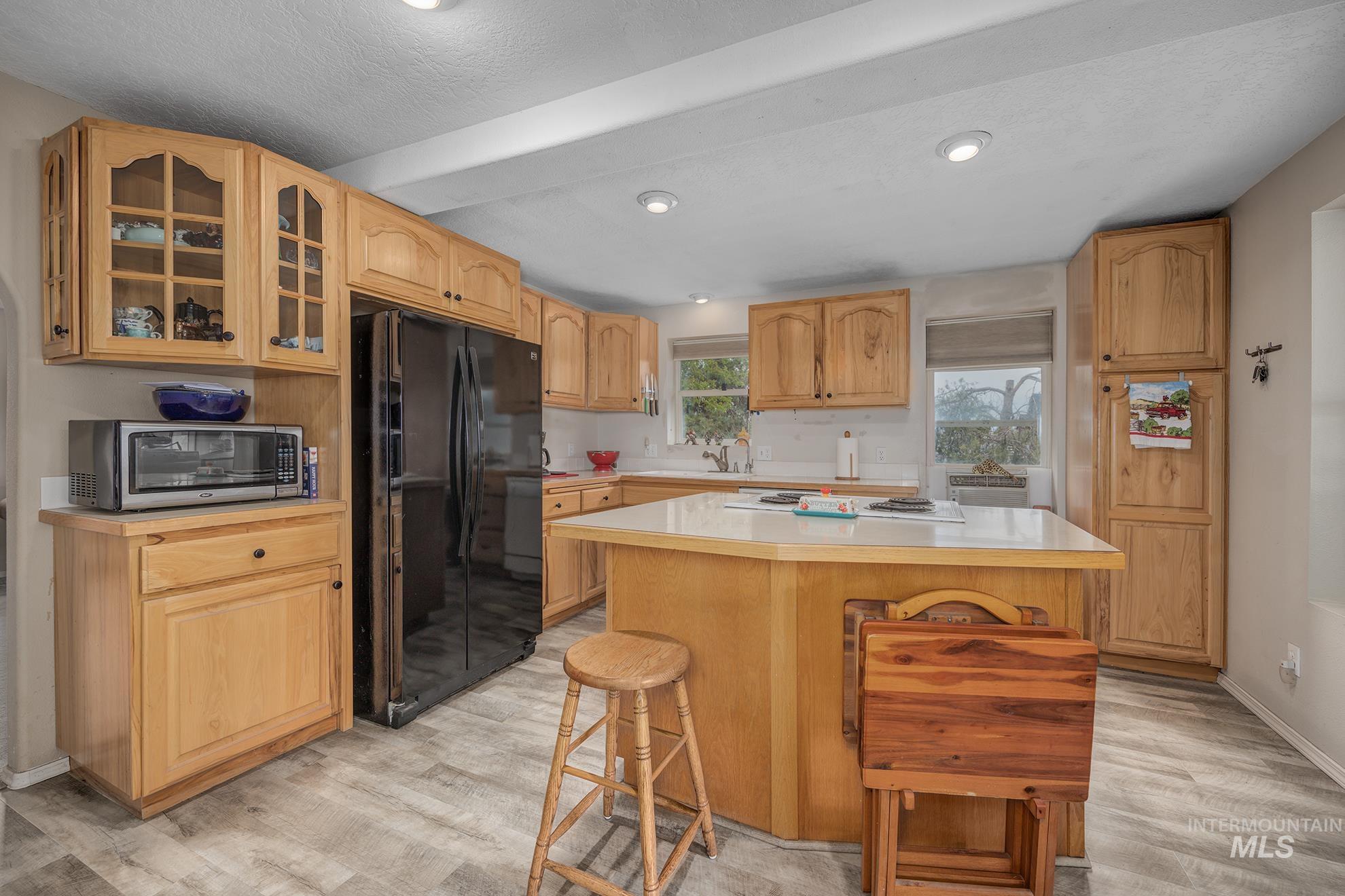 Kitchen featuring glass fronted cabinets, light countertops, freestanding refrigerator, and light wood finished floors