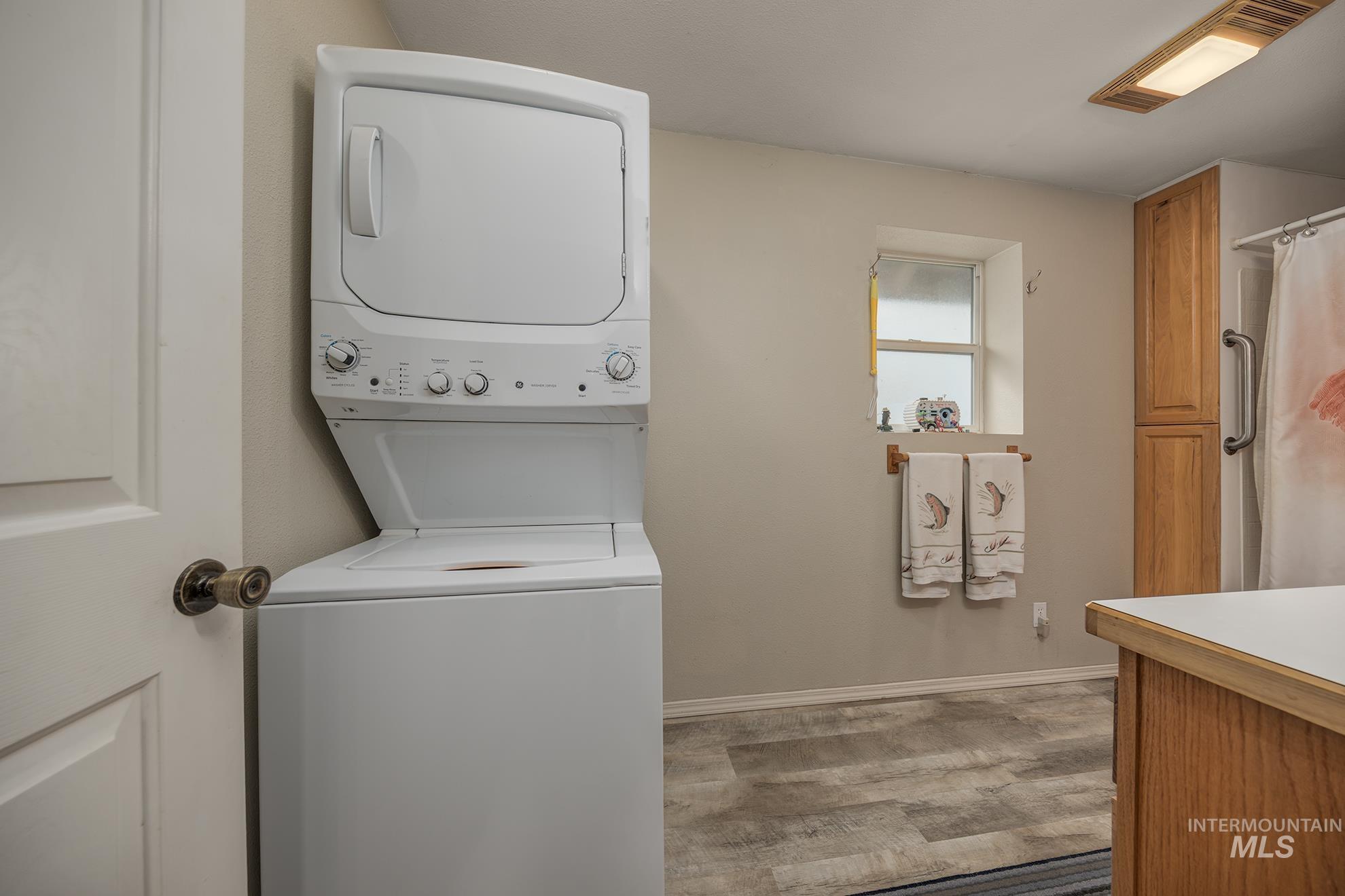 Laundry area with stacked washer and clothes dryer and light wood-style floors