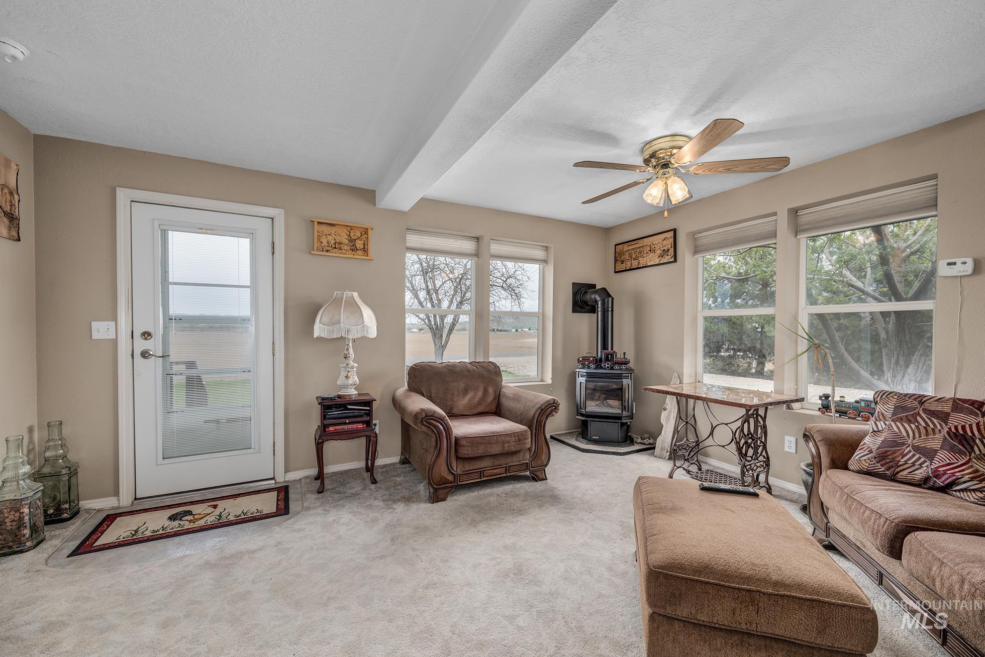 Living room with a wood stove, beamed ceiling, light colored carpet, a ceiling fan, and a textured ceiling