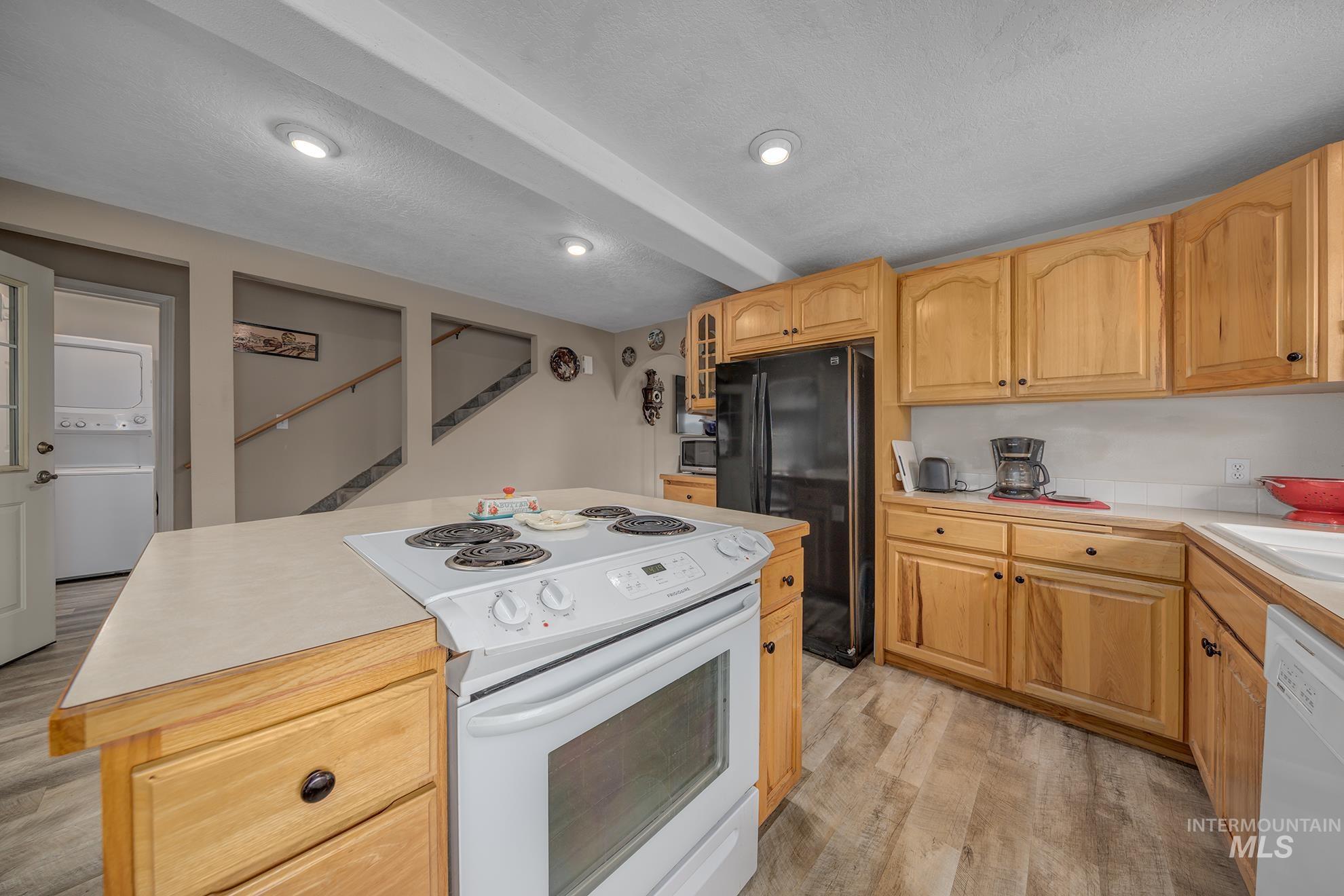Kitchen featuring white appliances, a center island, light wood-style floors, glass fronted cabinets, and stacked washing machine and dryer