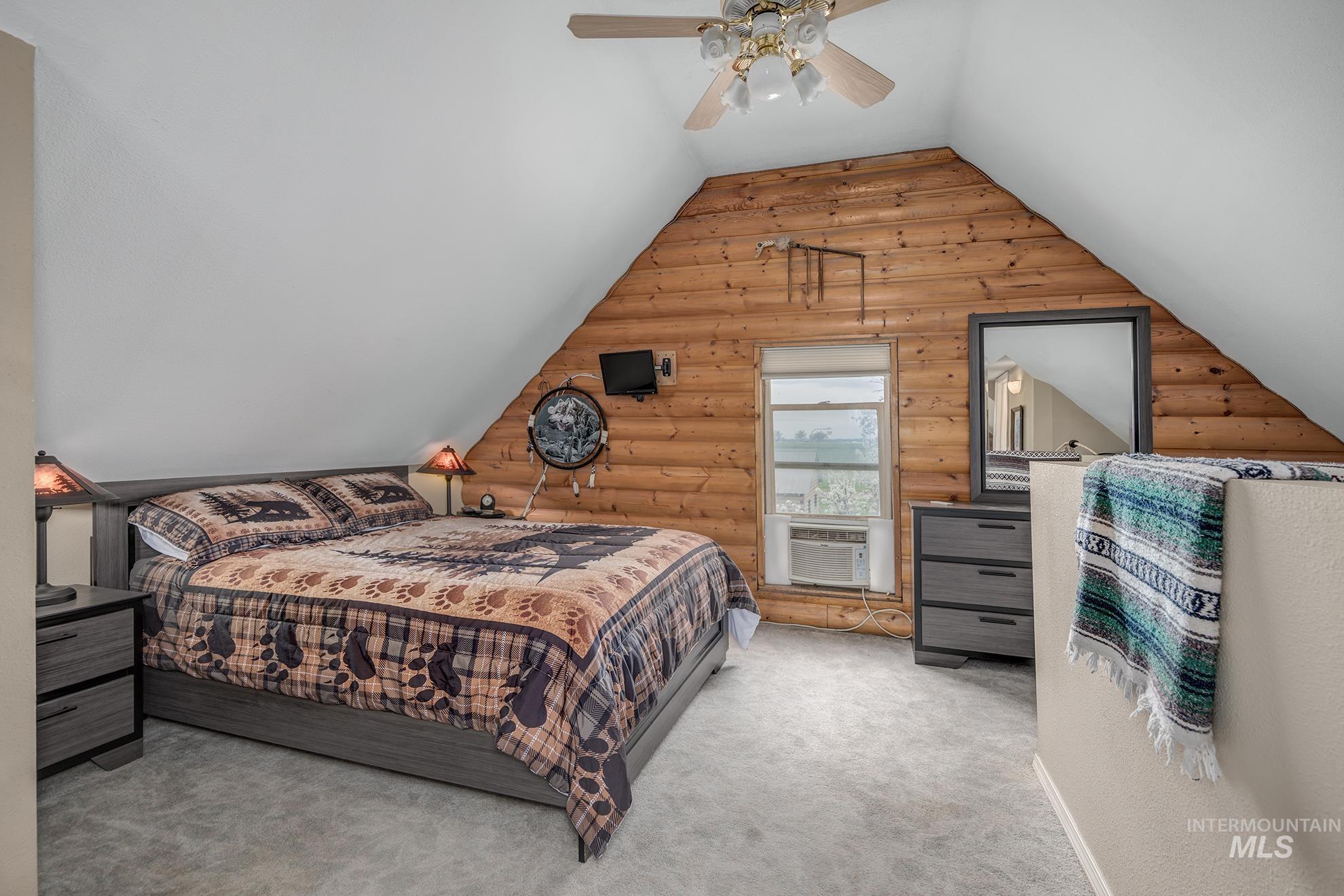 Bedroom with rustic walls, light carpet, ceiling fan, and lofted ceiling