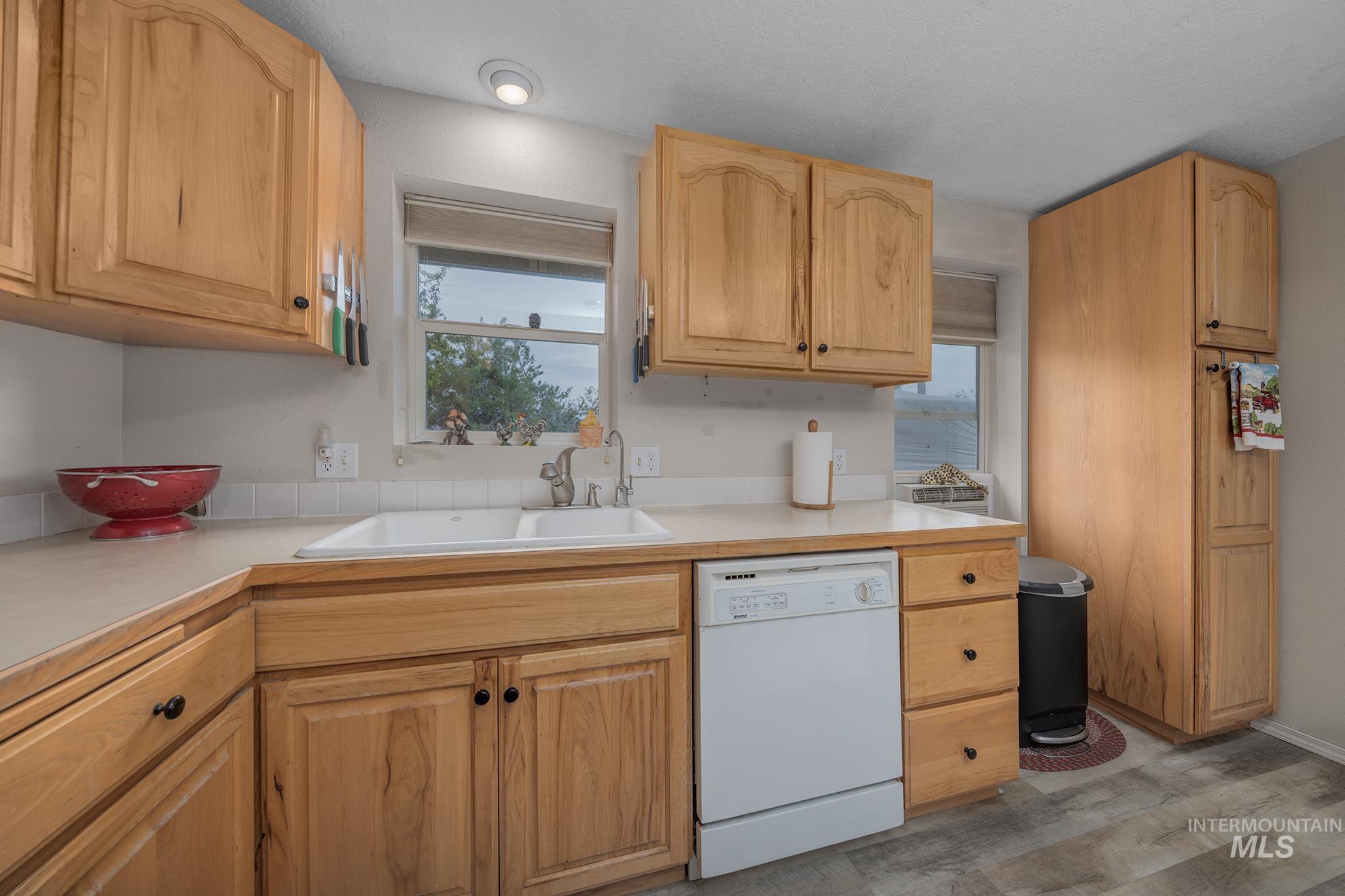 Kitchen with light countertops, white dishwasher, light wood-style floors, and light wood finish cabinets
